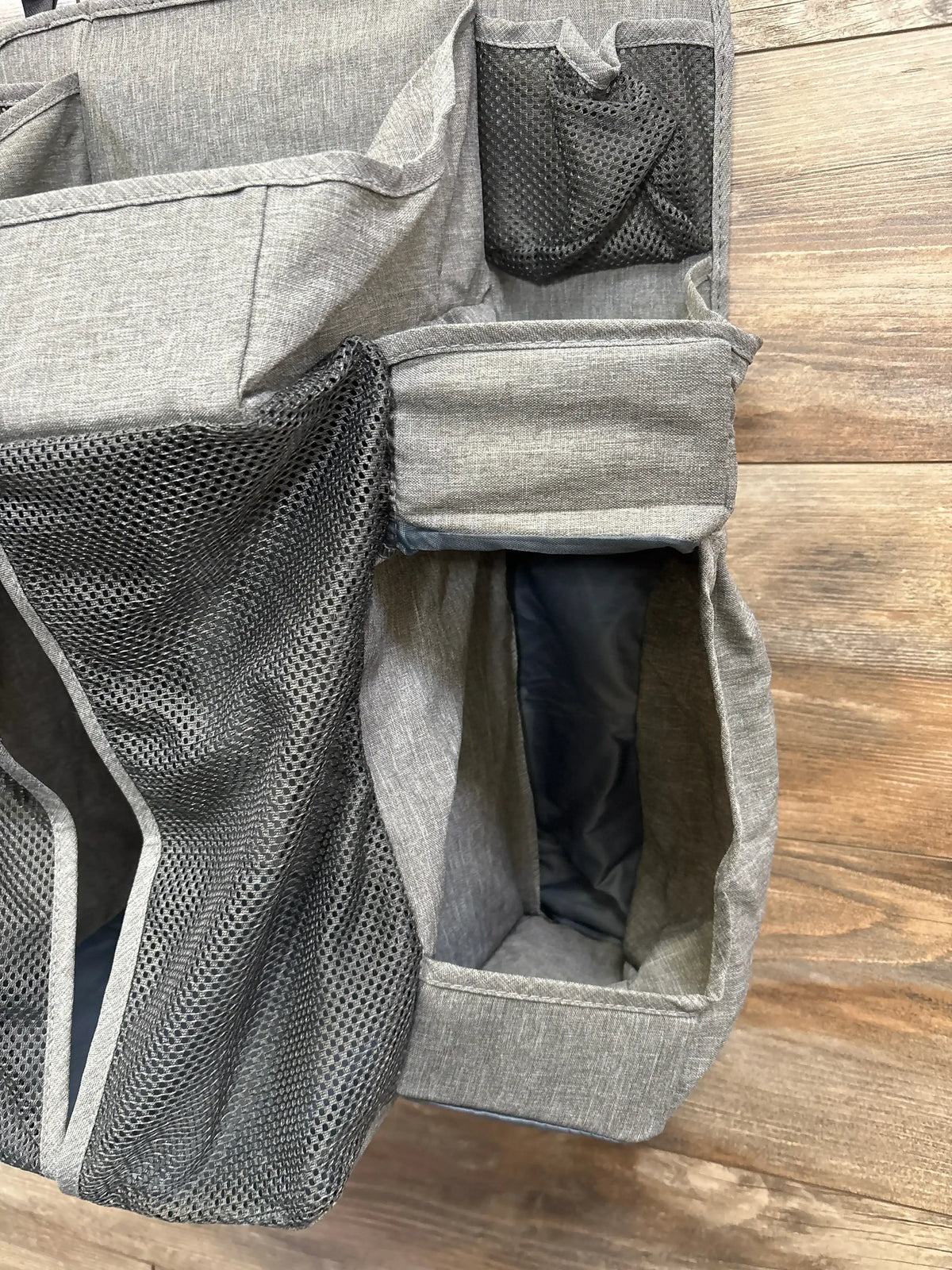 Close-up of Bizzu hanging diaper caddy organizer in grey showcasing mesh side pockets and open compartments on wood plank floor