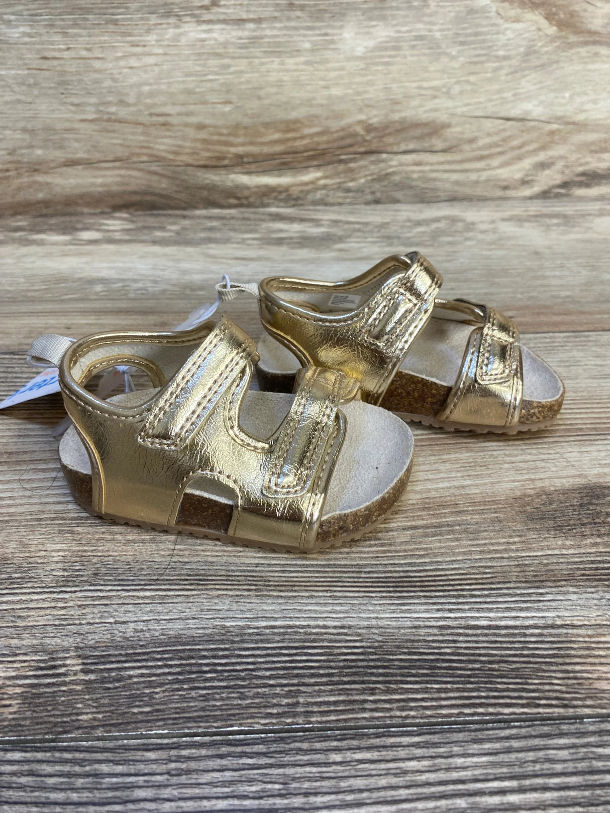 Gold toddler sandals with cork soles and Velcro straps on wood background