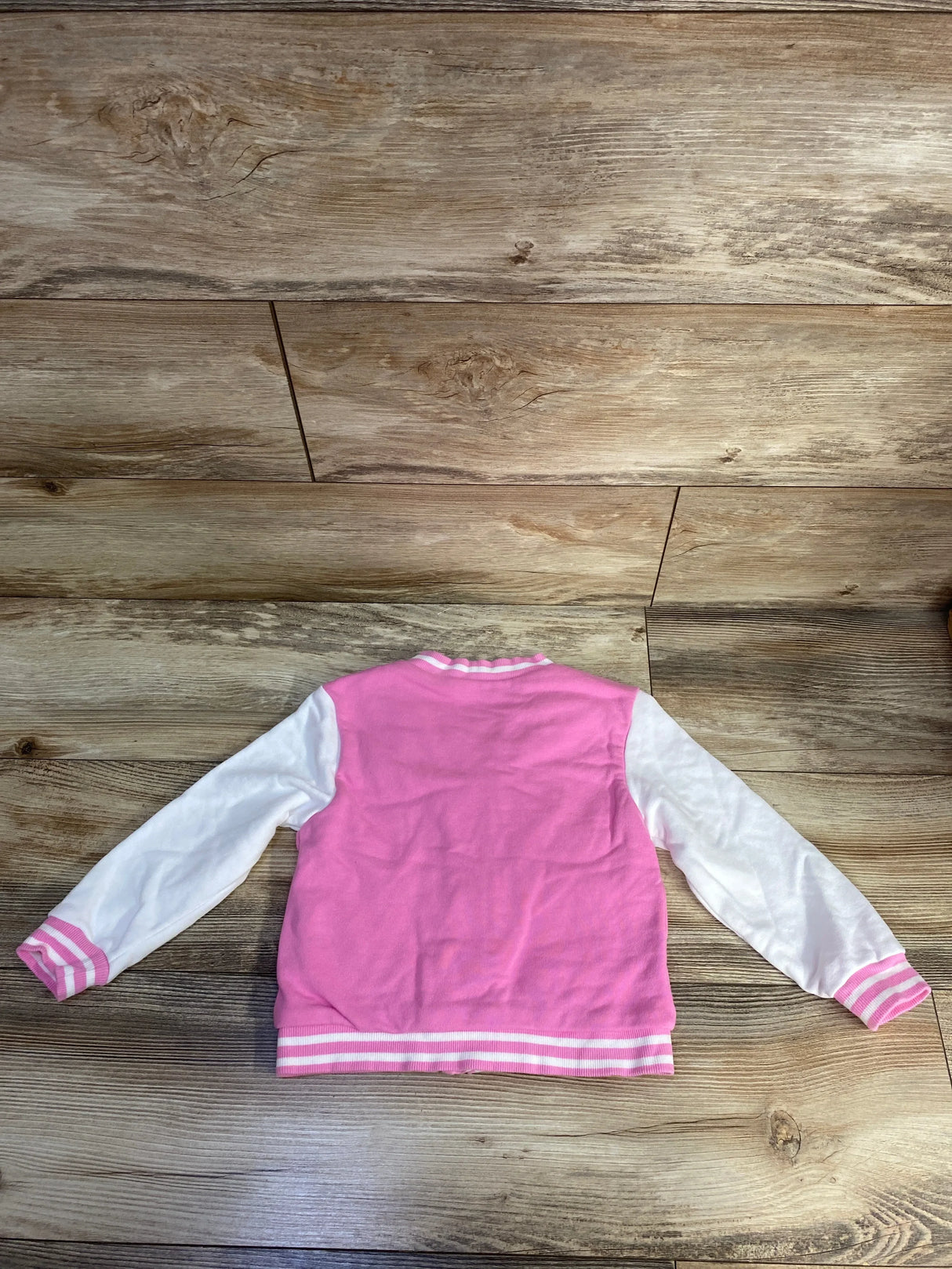Pink and white varsity jacket for kids on wooden floor background