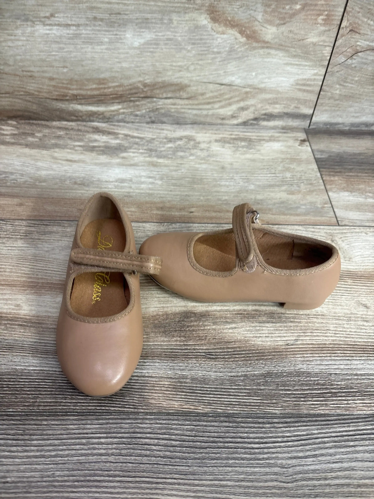 Top-down view of tan children's tap shoes (size 9C) showcasing Mary Jane strap and low heel on a wood-look floor