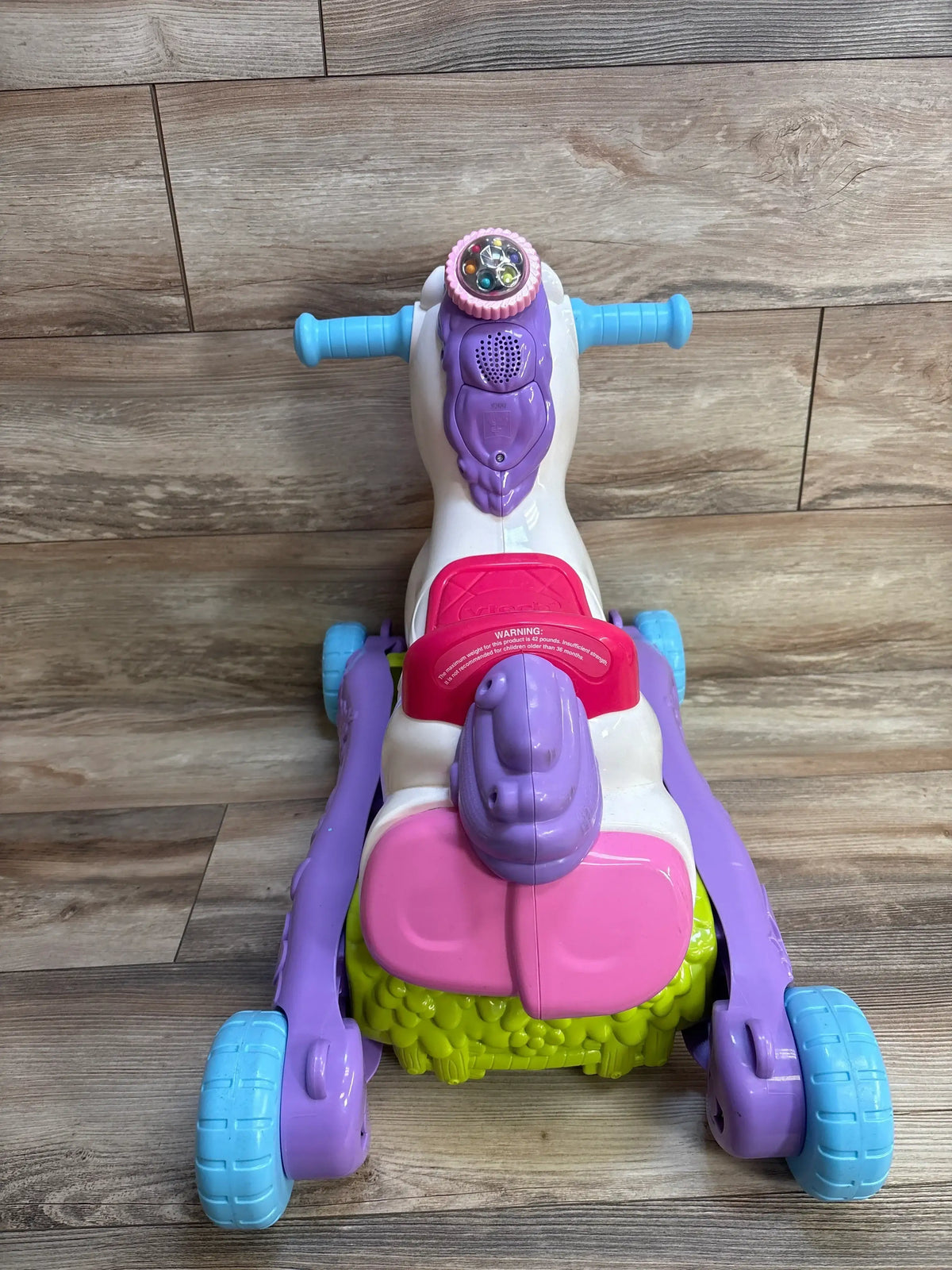 Front view of VTech Prance And Rock Learning Unicorn ride-on showing light-up head, interactive buttons, pink seat on wood floor