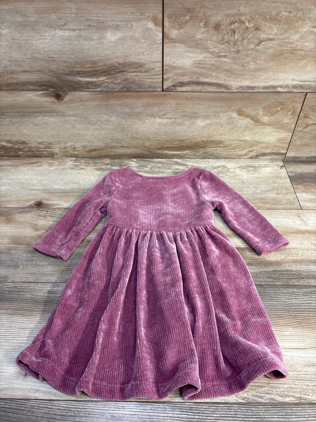 Flat-lay of pink velvet toddler dress (size 3T) showing long sleeves, gathered waist and full skirt on wood background