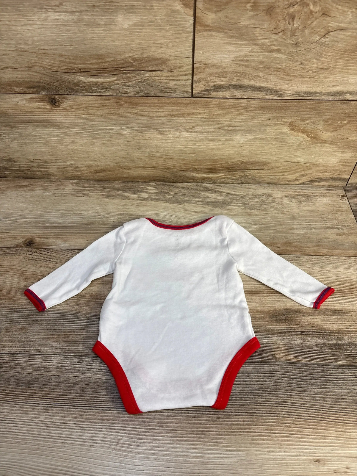 Back view of white long-sleeve baby bodysuit with red trim, size 3M, laid flat on wooden surface