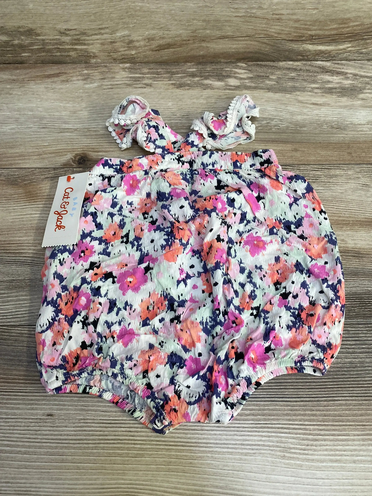 Flat lay of Cat and Jack newborn floral romper with flutter ruffle straps and elastic leg openings on wood background