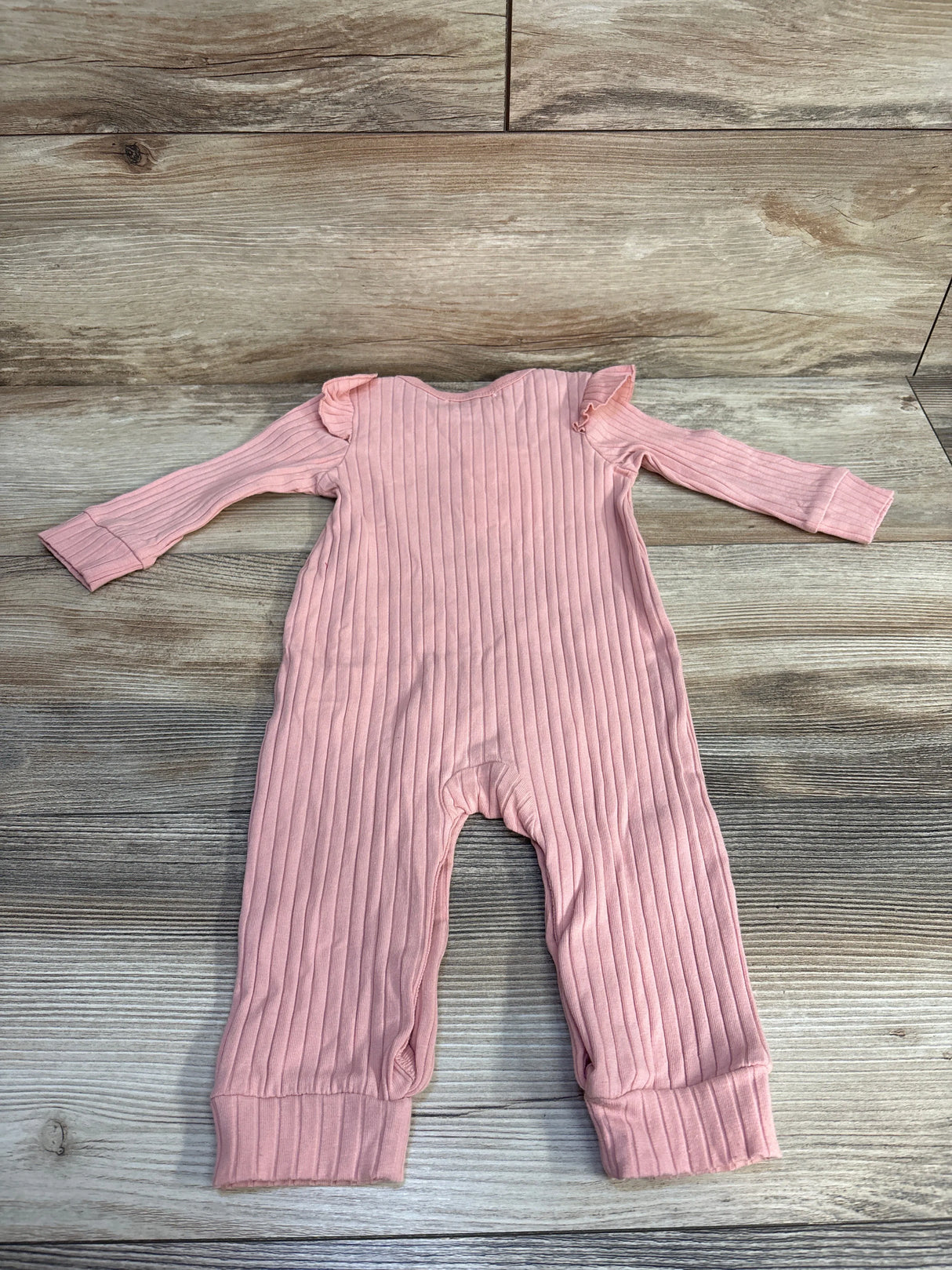 Pink ribbed baby romper with long sleeves and ruffle details on shoulders on wood floor