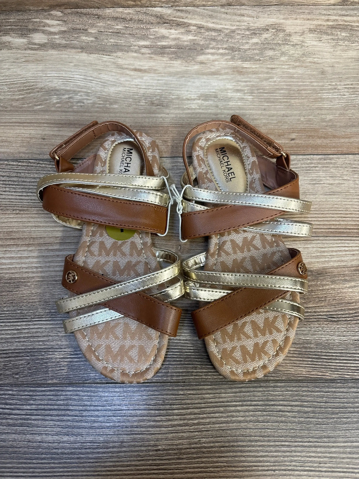 Toddler sandals with gold and brown straps on wood floor, MK logo pattern insole