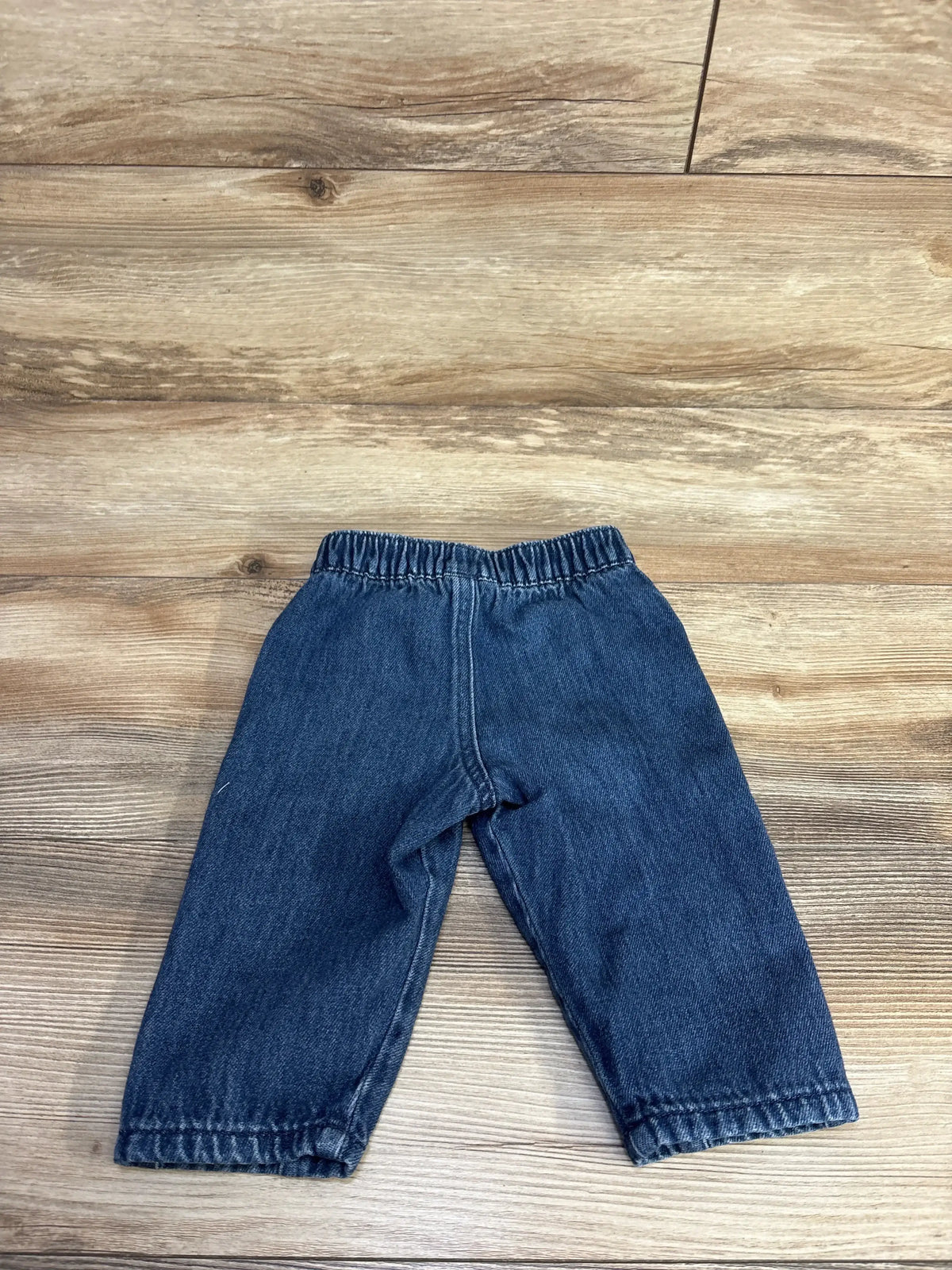 Front view of Easy Peasy pull-on baby jeans (12 months) showing elastic waistband and straight legs on wood background