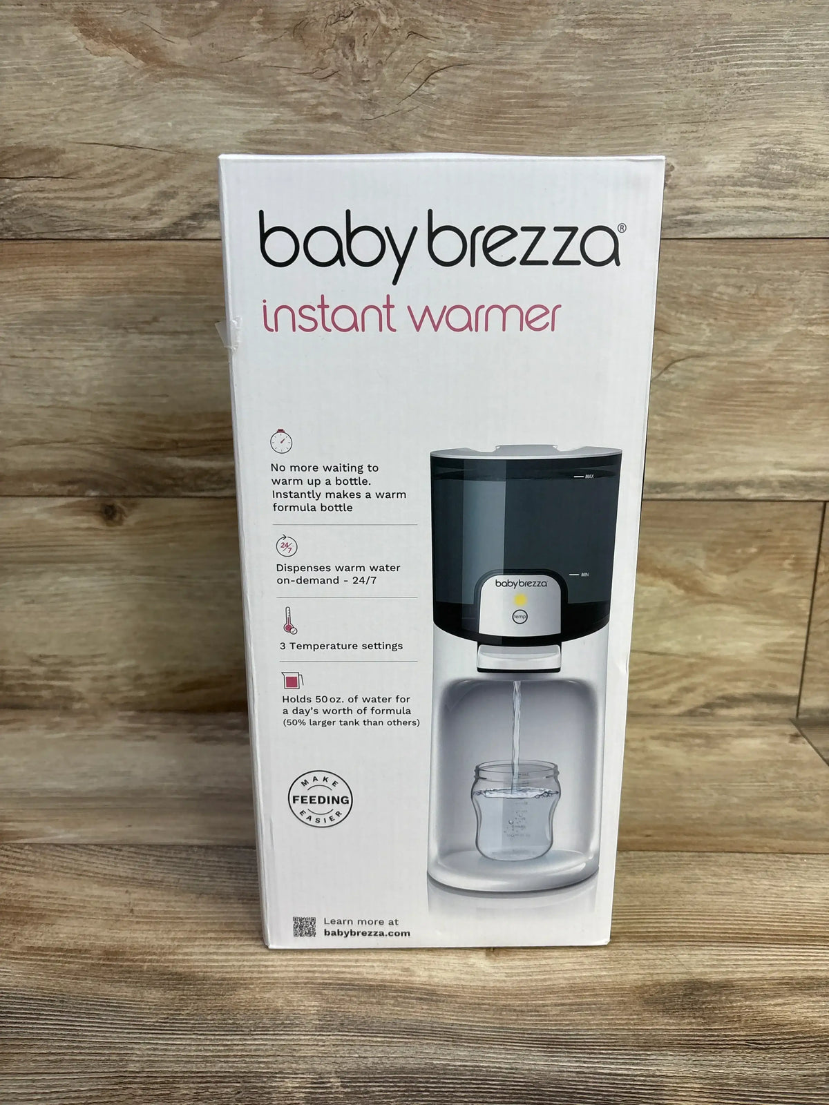 Front view of Baby Brezza Instant Bottle Warmer in white in original sealed retail box with product illustration on wood plank floor