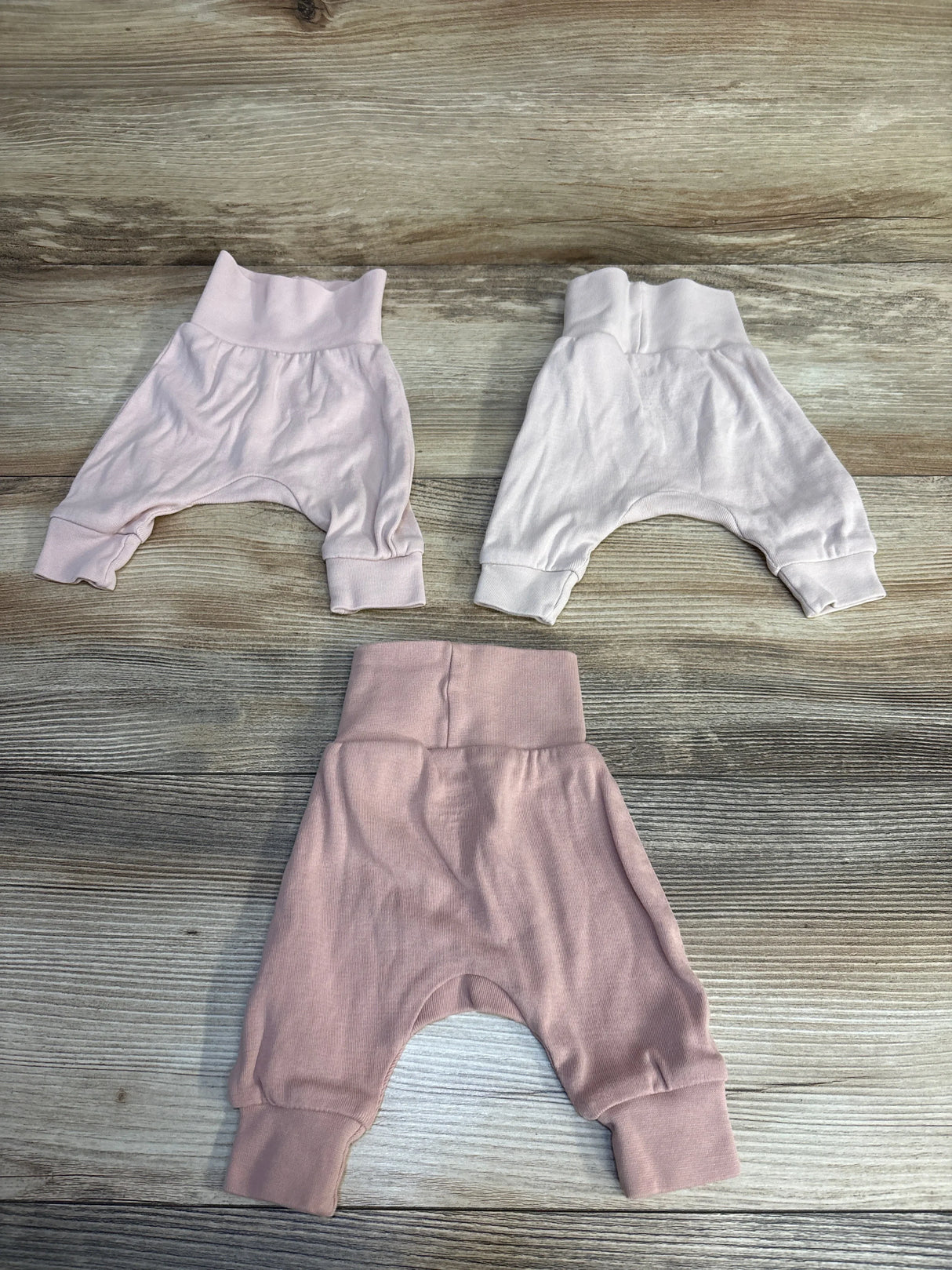 Soft baby harem pants in pink, white, and mauve, laid on wood floor for resale