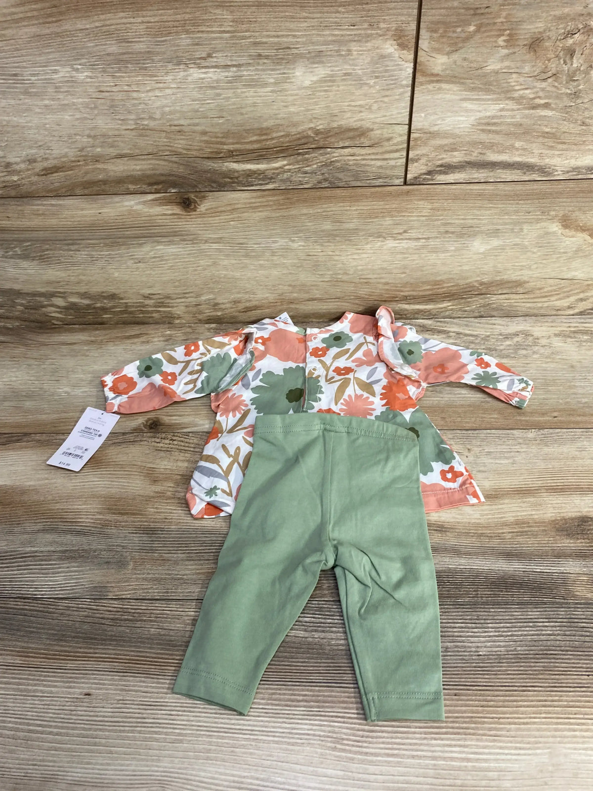 Baby outfit with floral long-sleeve top and green leggings on wooden floor, kids clothes resale