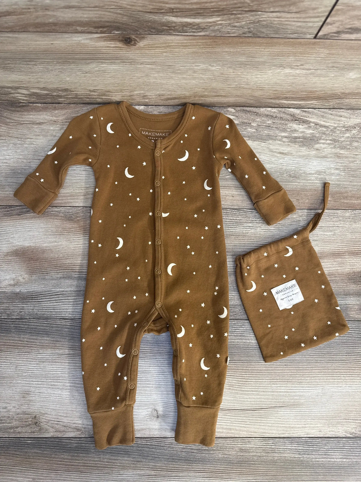 Front view of MakeMake Organics snap-front moon and stars brown sleeper with matching drawstring bag on wood background