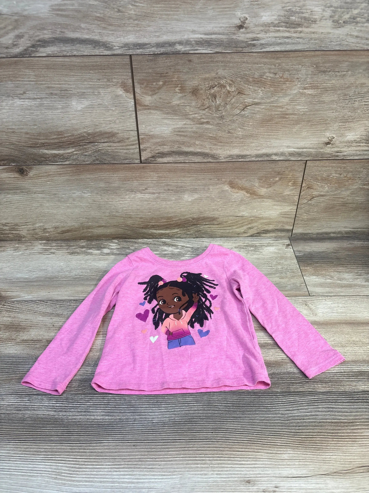 Front view of Children’s Place pink long-sleeve toddler shirt showcasing cartoon girl graphic and hearts on wood floor background