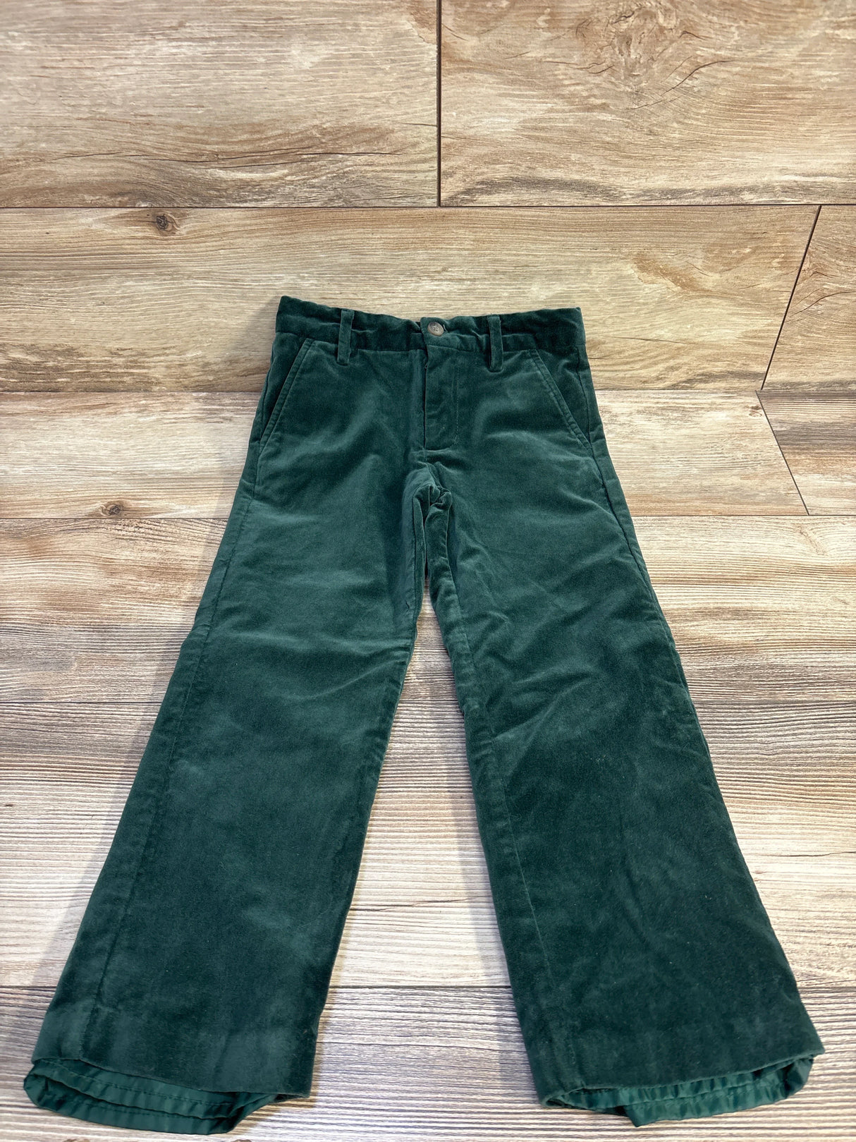 Flat lay of Janie and Jack velvet pants showing pine green velvet fabric, front pockets and slight flare on wood background