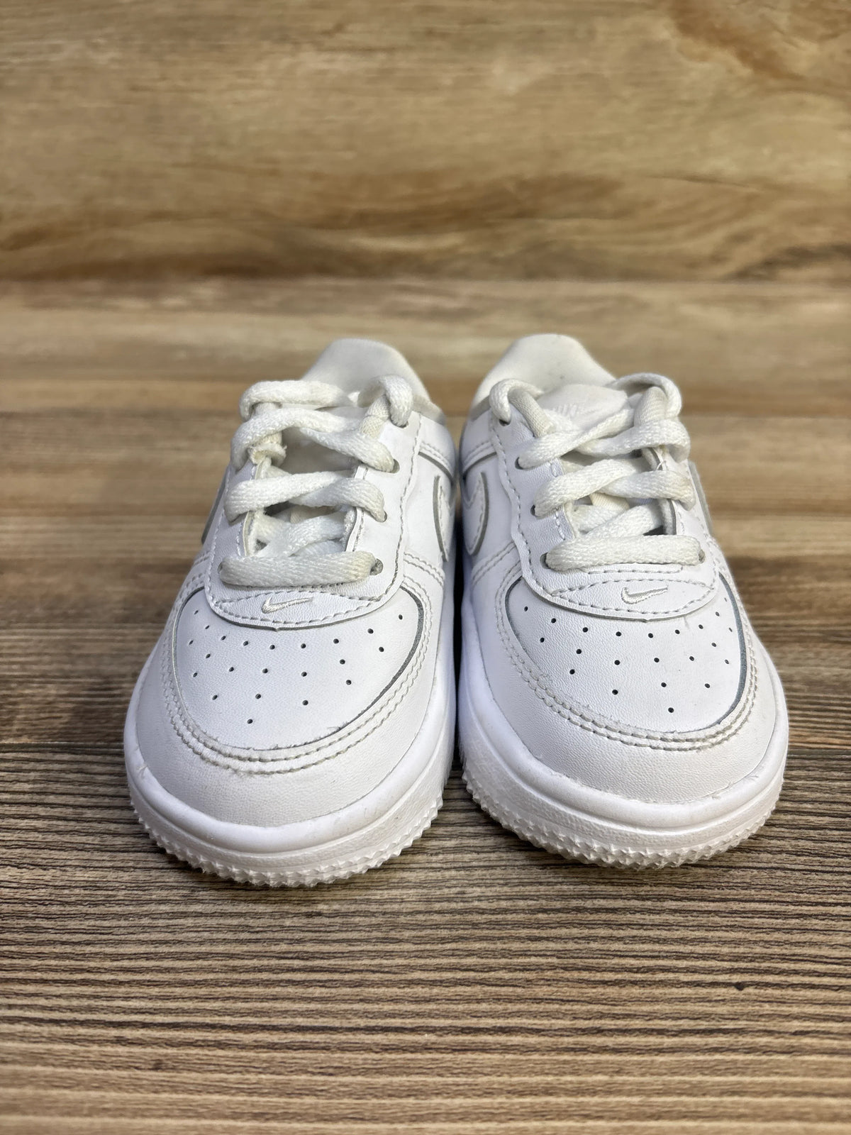 Front view of toddler Nike Air Force 1 Low sneakers size 5C showing perforated toe, laces, and small Swoosh on wood surface