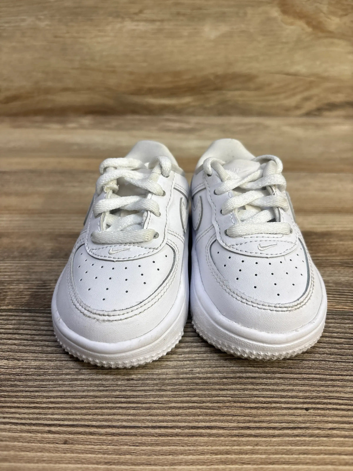 Front view of toddler Nike Air Force 1 Low sneakers size 5C showing perforated toe, laces, and small Swoosh on wood surface