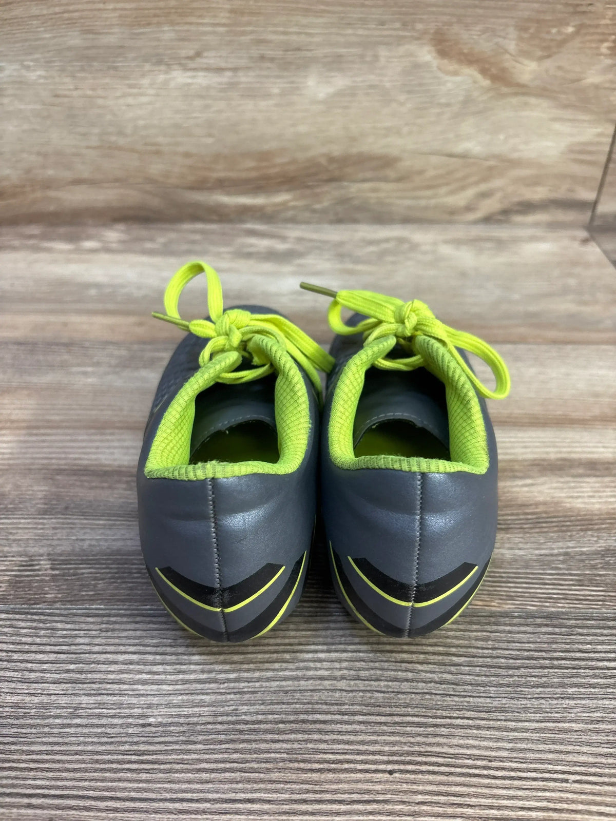 Rear view of Hawkwell Athletic toddler gray soccer cleats showcasing neon yellow-green lining and laces on wood-grain surface
