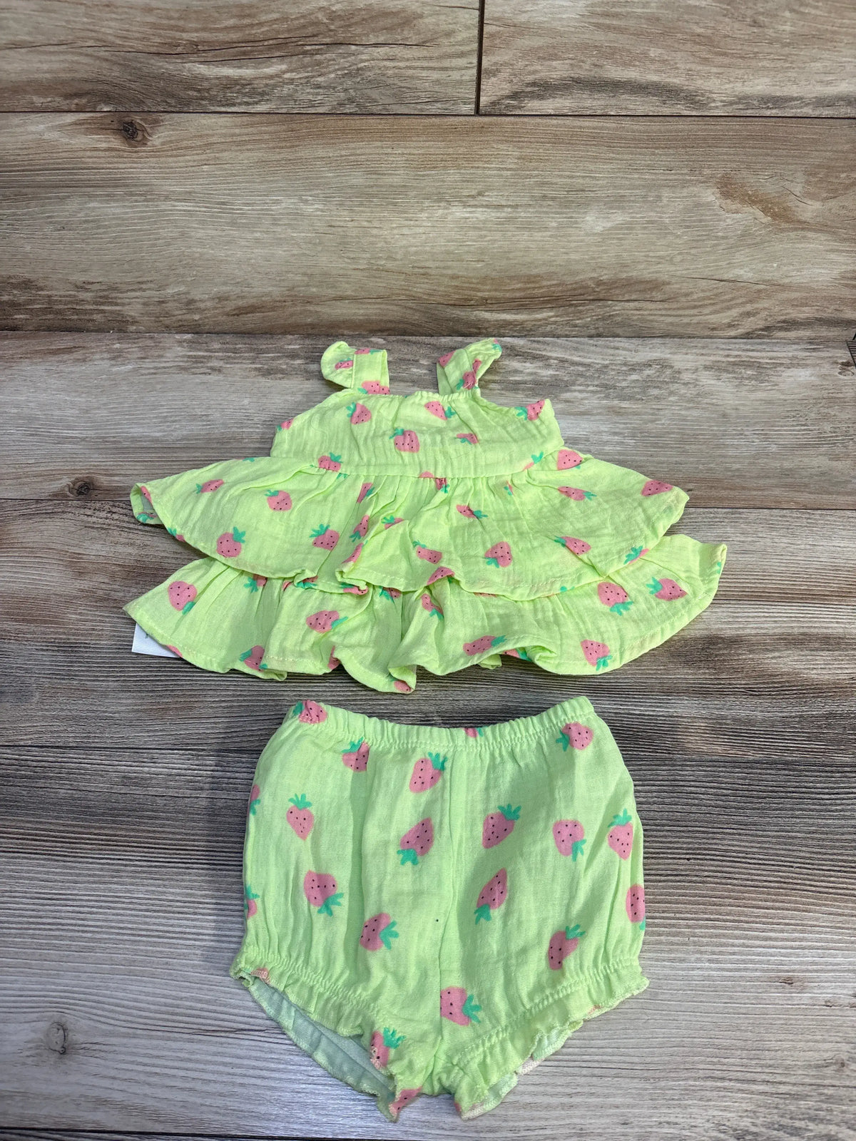 Flat lay of green strawberry-print two-piece dress and bloomers with ruffled tiers and elastic waist on wood background