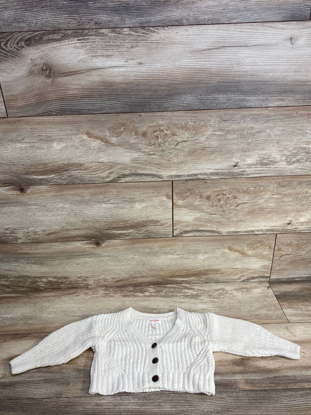 White knitted baby cardigan with three brown buttons laid on wooden floor