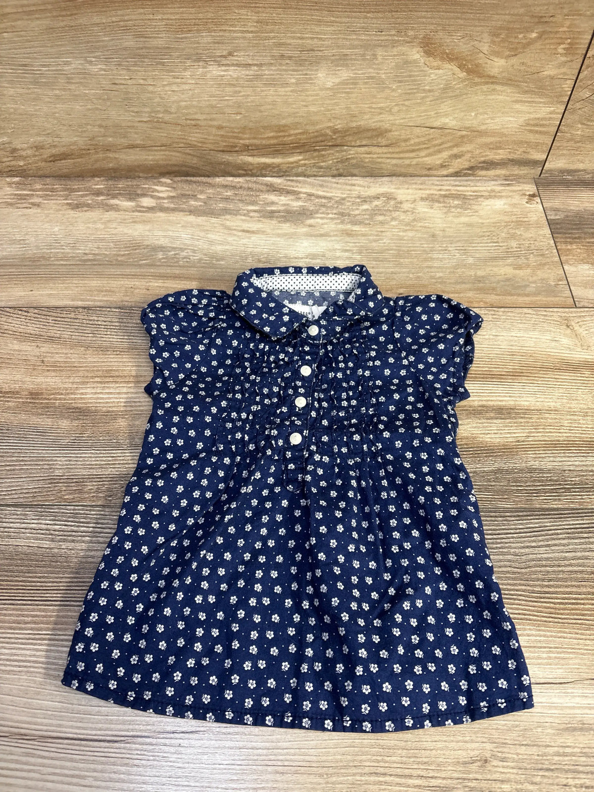 Front view of H&M navy floral collared shirt dress for 6 to 9 months, with gathered waist and white buttons on wood flooring