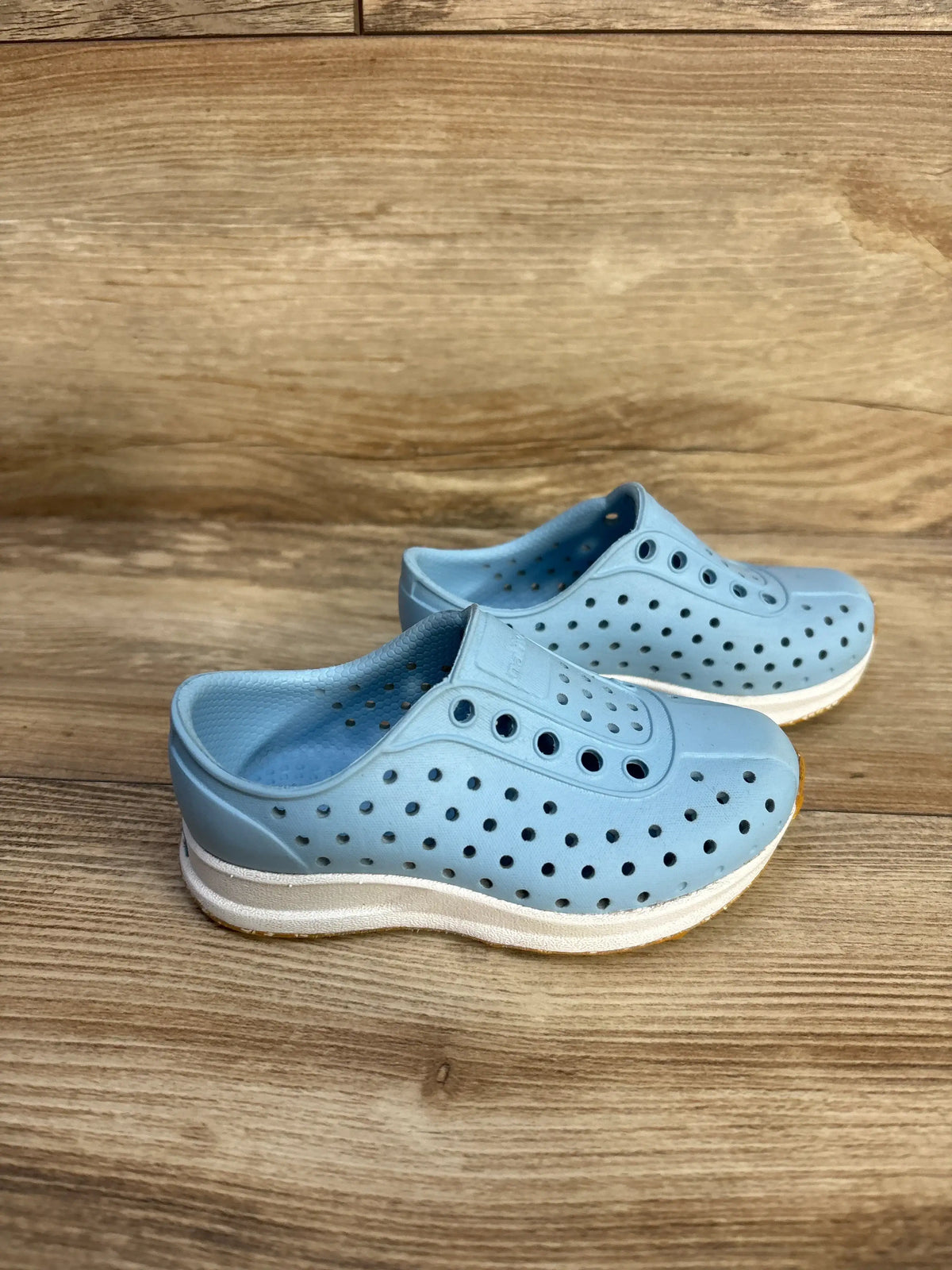 Pair of light blue Native Robbie Sugarlite slip-on shoes for kids on a wooden surface.