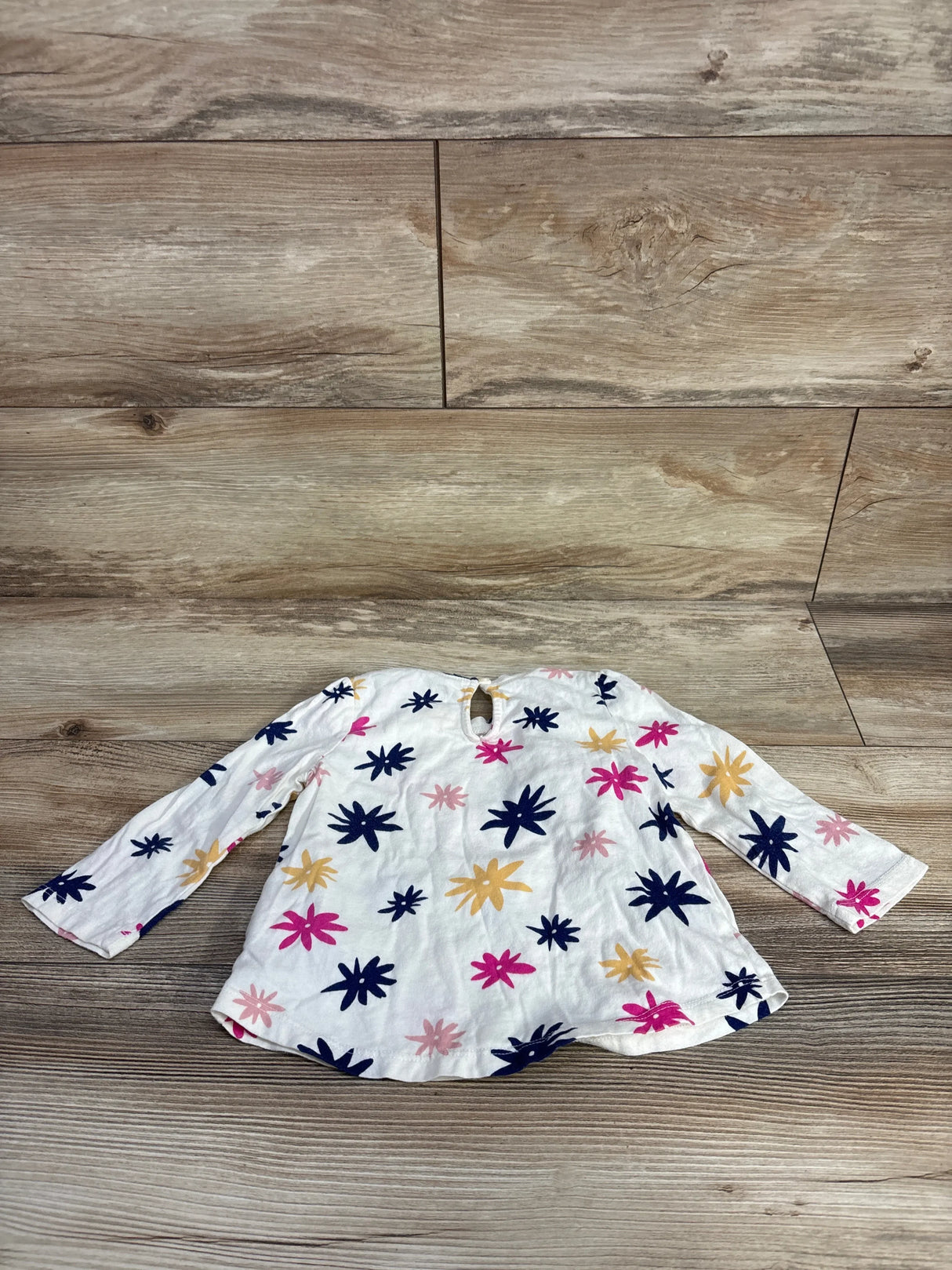 White long-sleeve toddler shirt with pink, navy, and beige flower prints on wooden floor