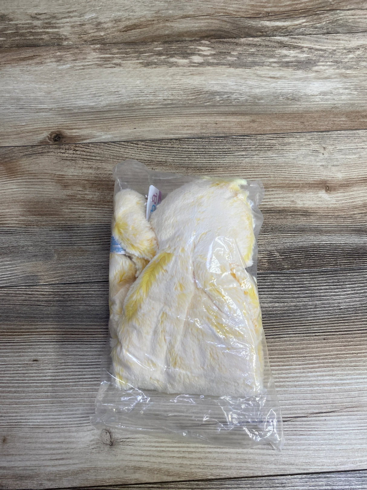Yellow and white plush children's teddy bear toy wrapped in clear plastic on wooden surface