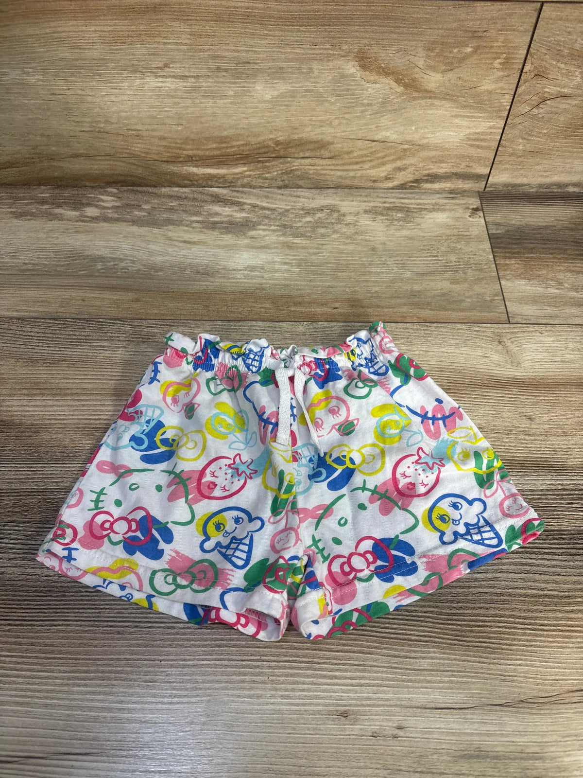 Front view of white Hello Kitty shorts, size 4T, with colorful character print and elastic waistband on wood floor