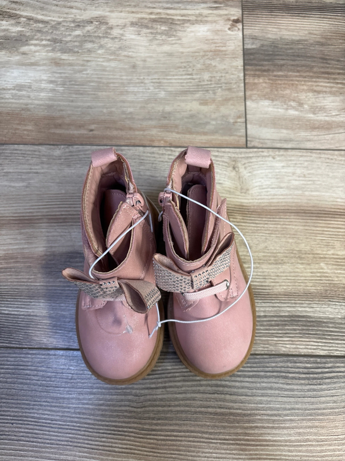 Top-down view of Jessica Simpson Daria toddler pink ankle boots, size 6C, showcasing rhinestone bow detail and side zippers on wood floor