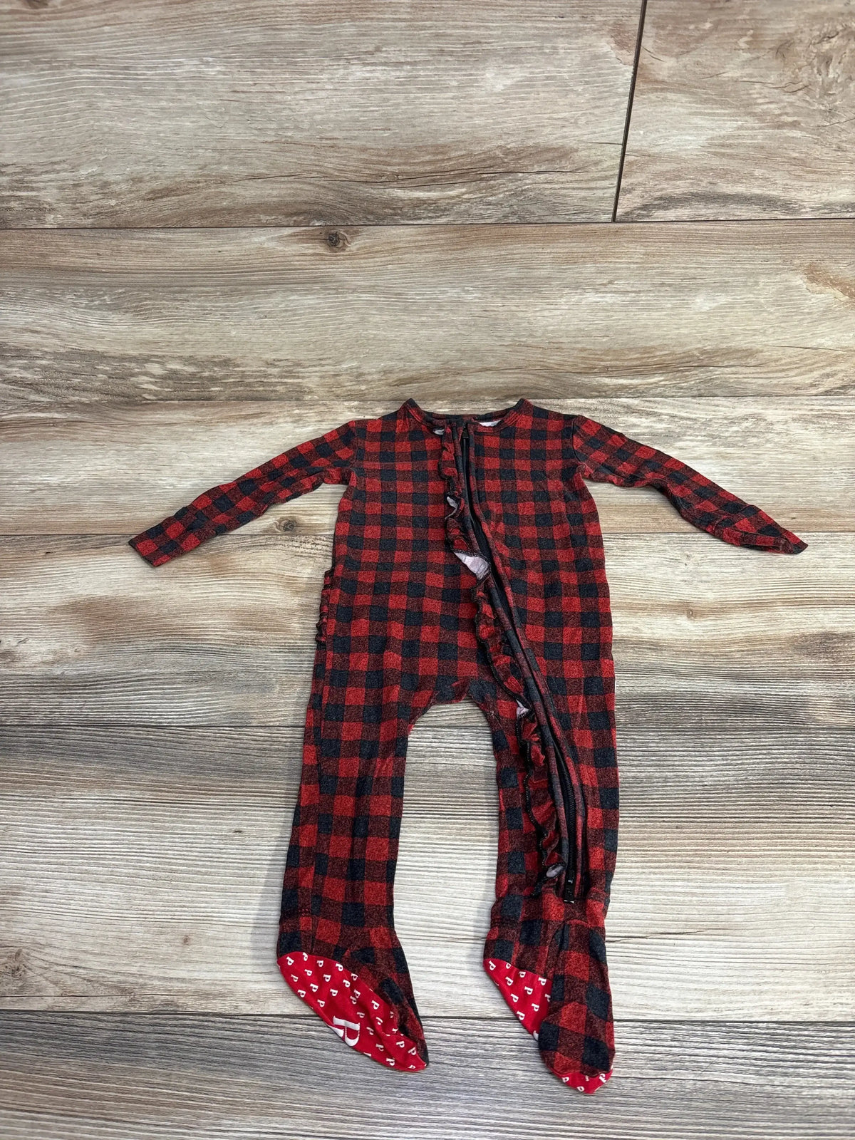 Red and black plaid baby sleeper footed pajamas with zipper on wood background
