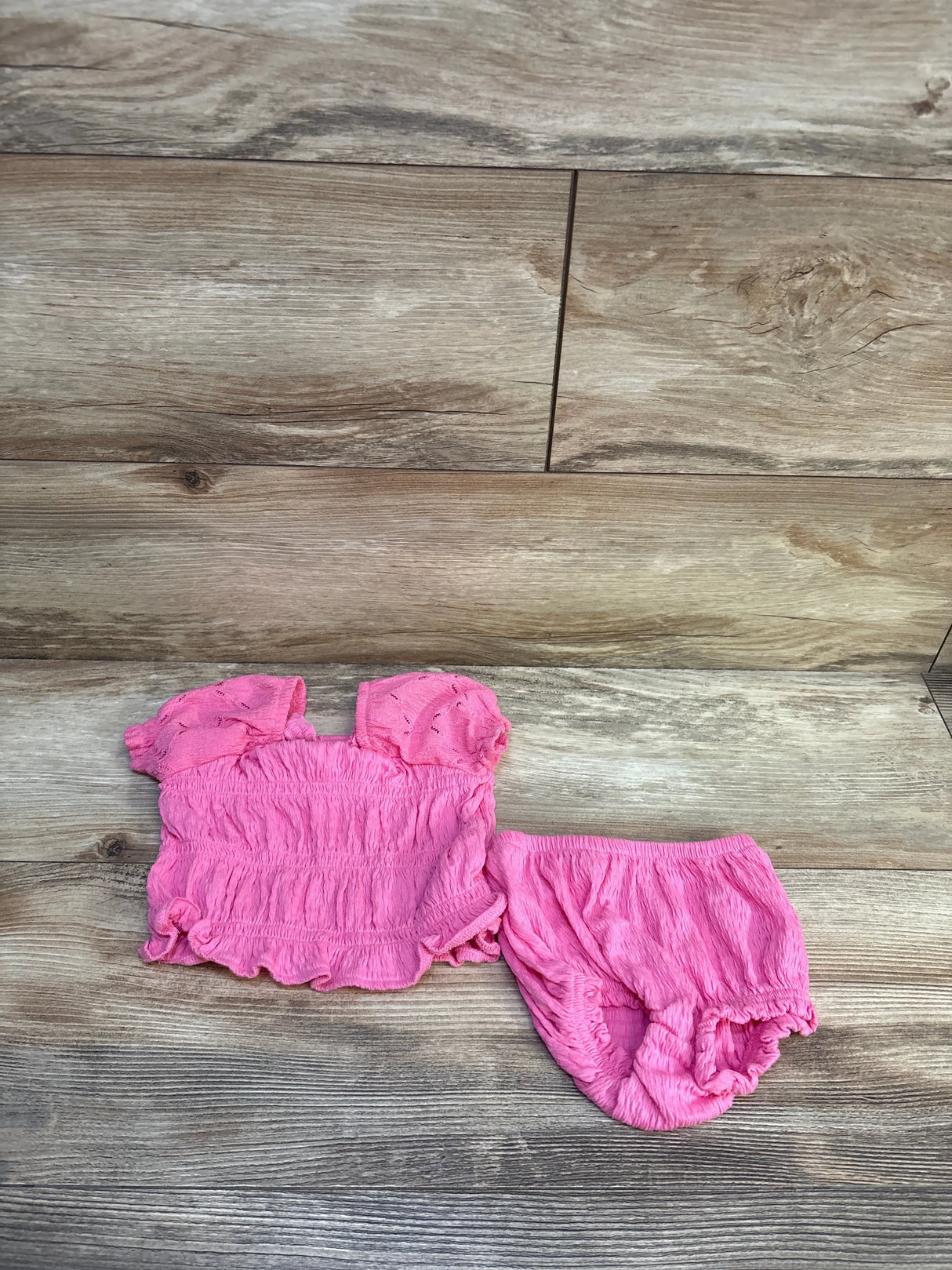 Pink baby ruffle top and bloomers set on wood background, gently used children's clothing