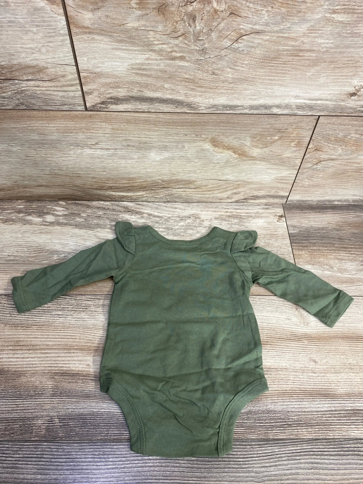 Green long-sleeve baby onesie with ruffle shoulder detail on wood background