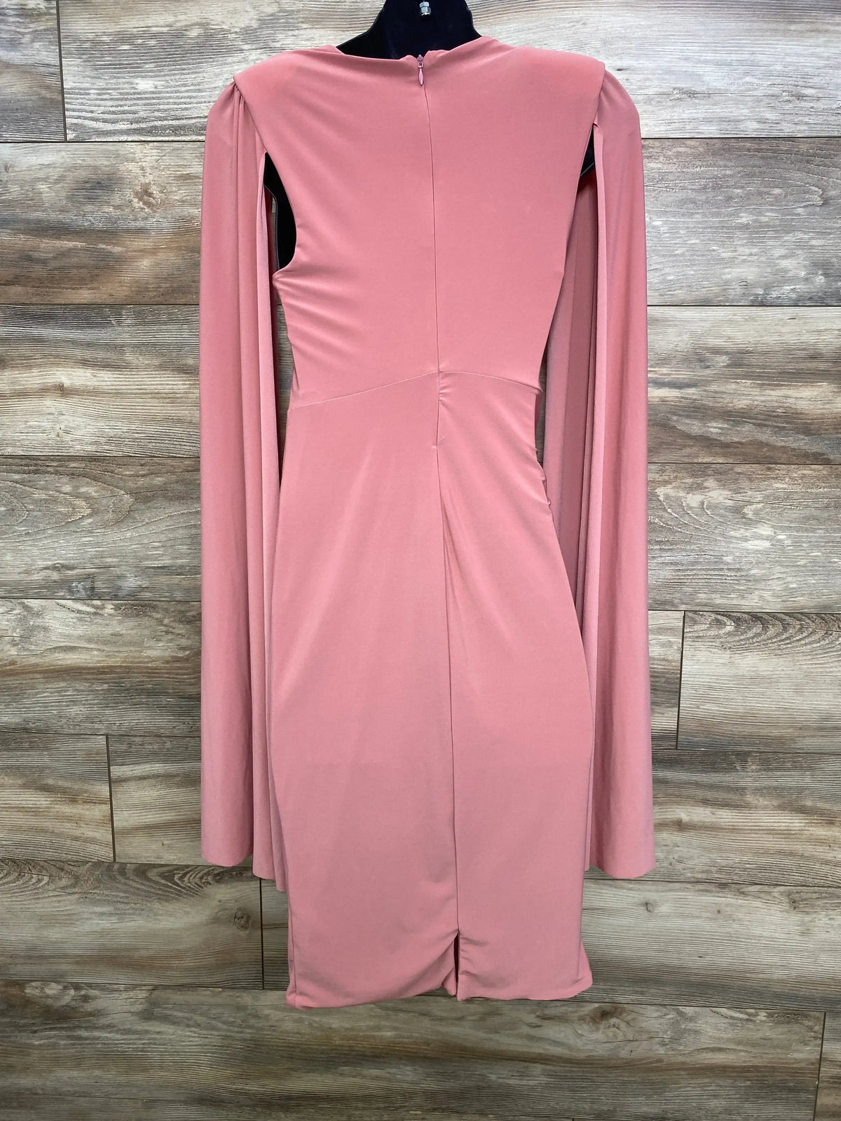 Back view of pink Club L London maternity dress showcasing long cape sleeves and center back zipper against wood panel background