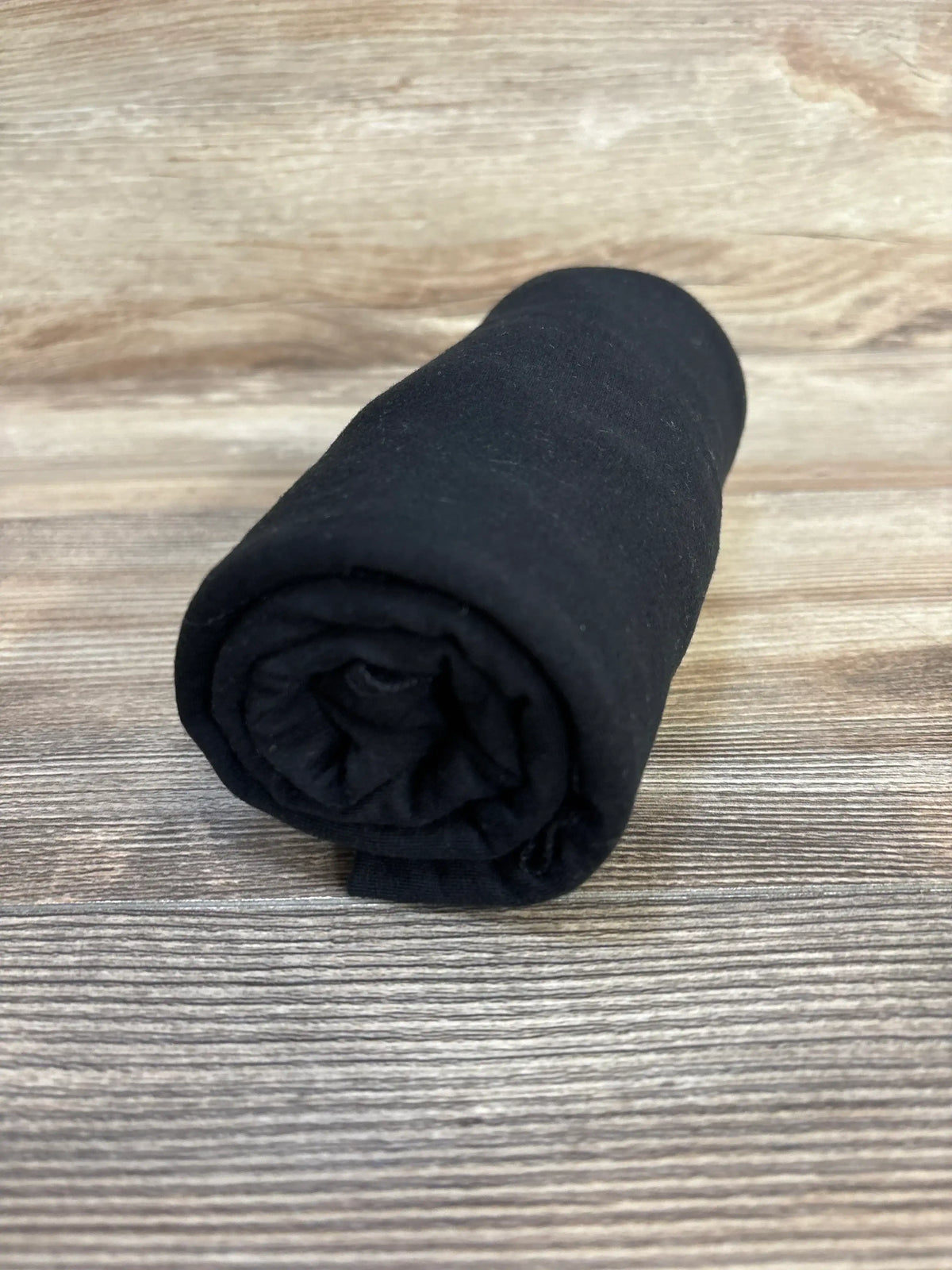 Rolled view of Copper Pearl Knit Swaddle Blanket in black showcasing soft knit texture on a wood-grain surface