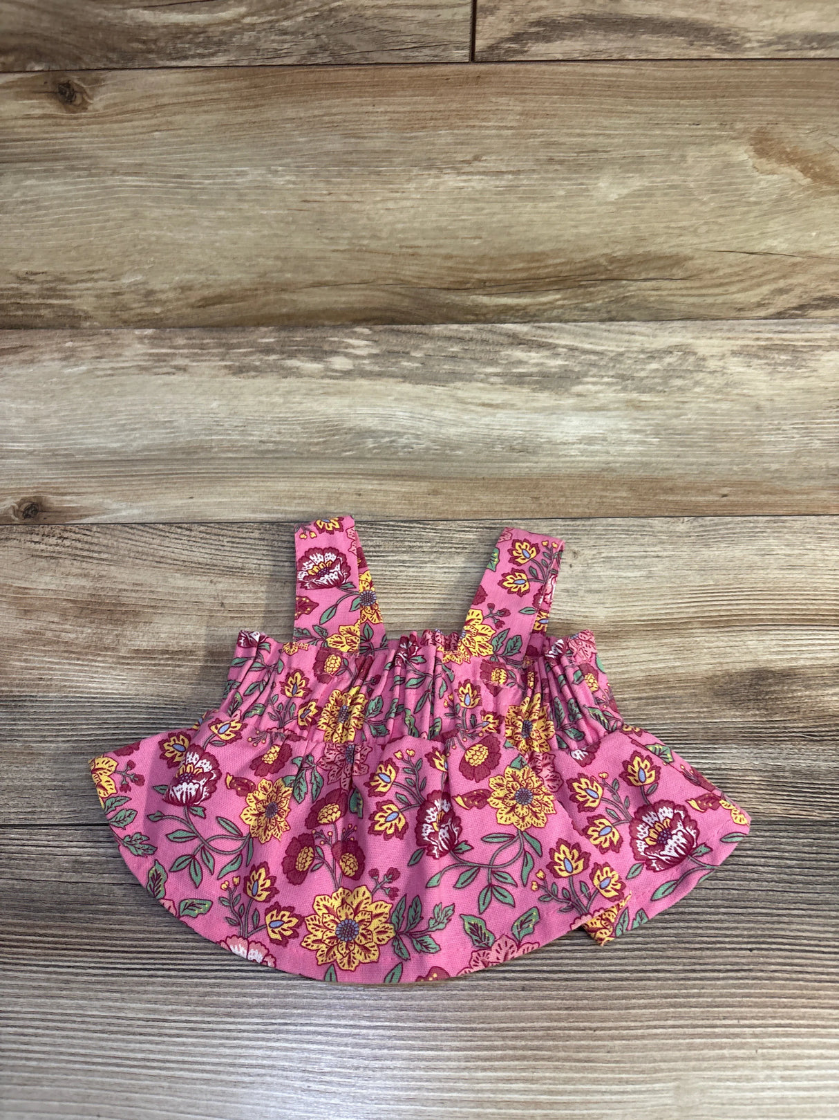 Front view of pink floral smocked cropped tank top showing smocked bodice, straps, and ruffled hem on wood background