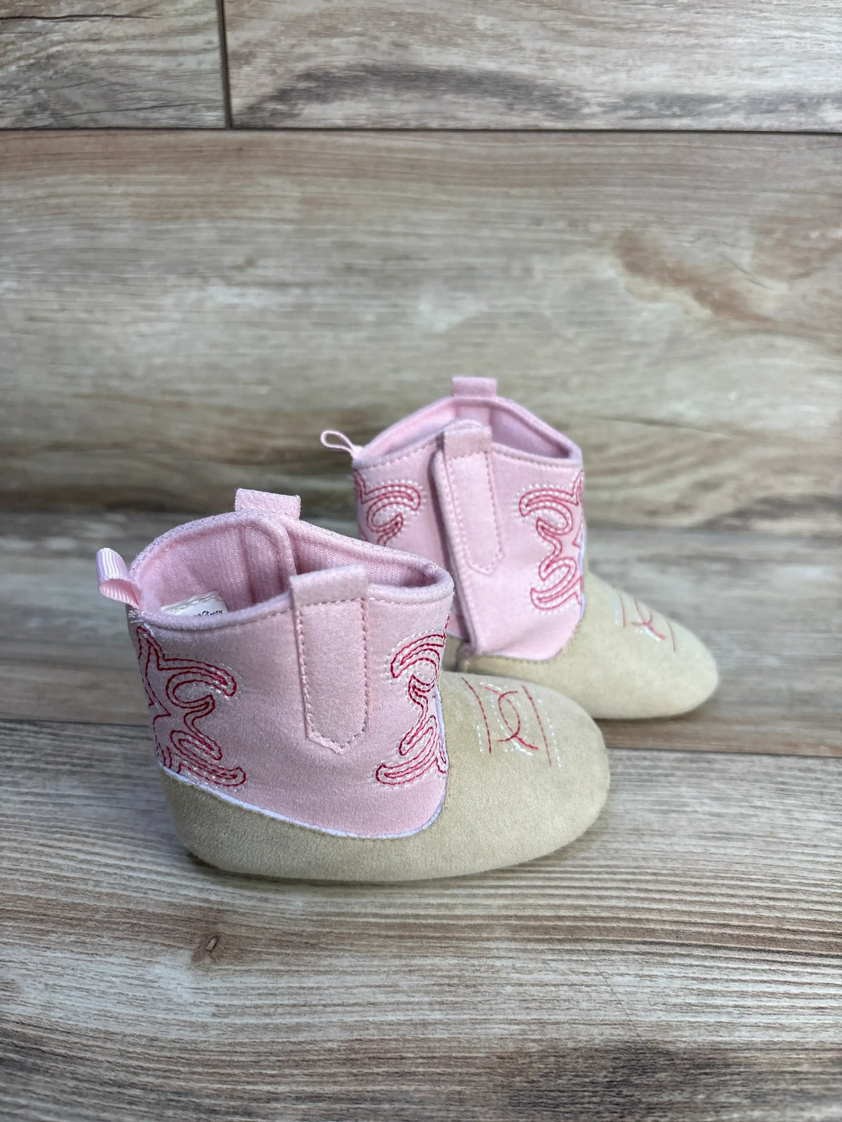 Pink Stepping Stones cowgirl crib boots for babies on a wooden surface