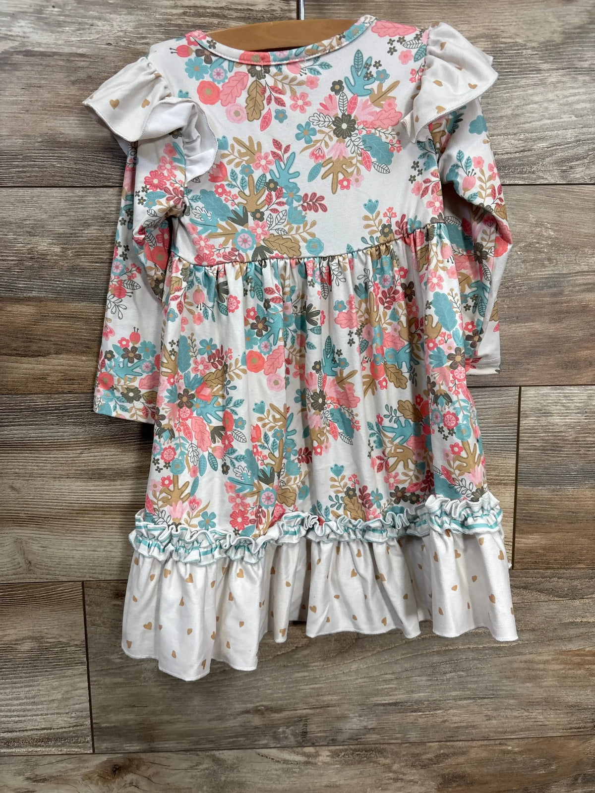 Girls long sleeve floral dress with ruffle trim and white heart-patterned hem on hanger