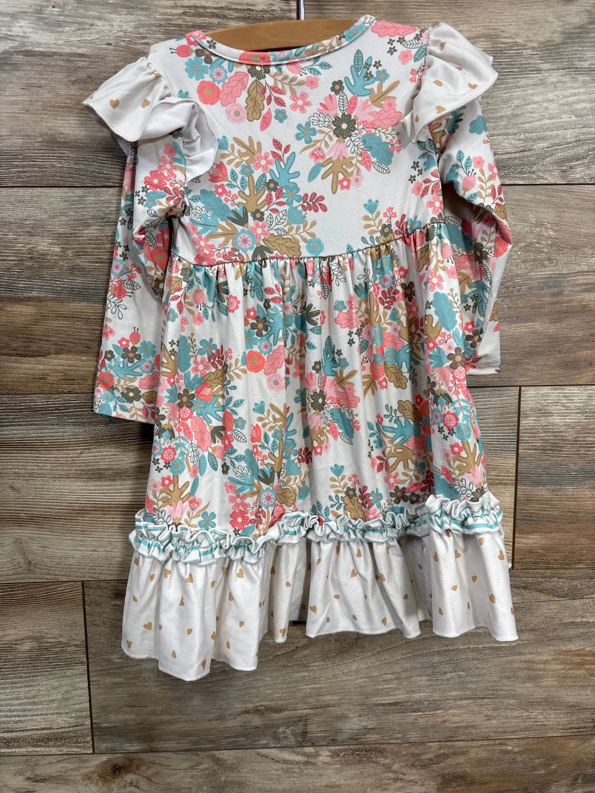 Girls long sleeve floral dress with ruffle trim and white heart-patterned hem on hanger