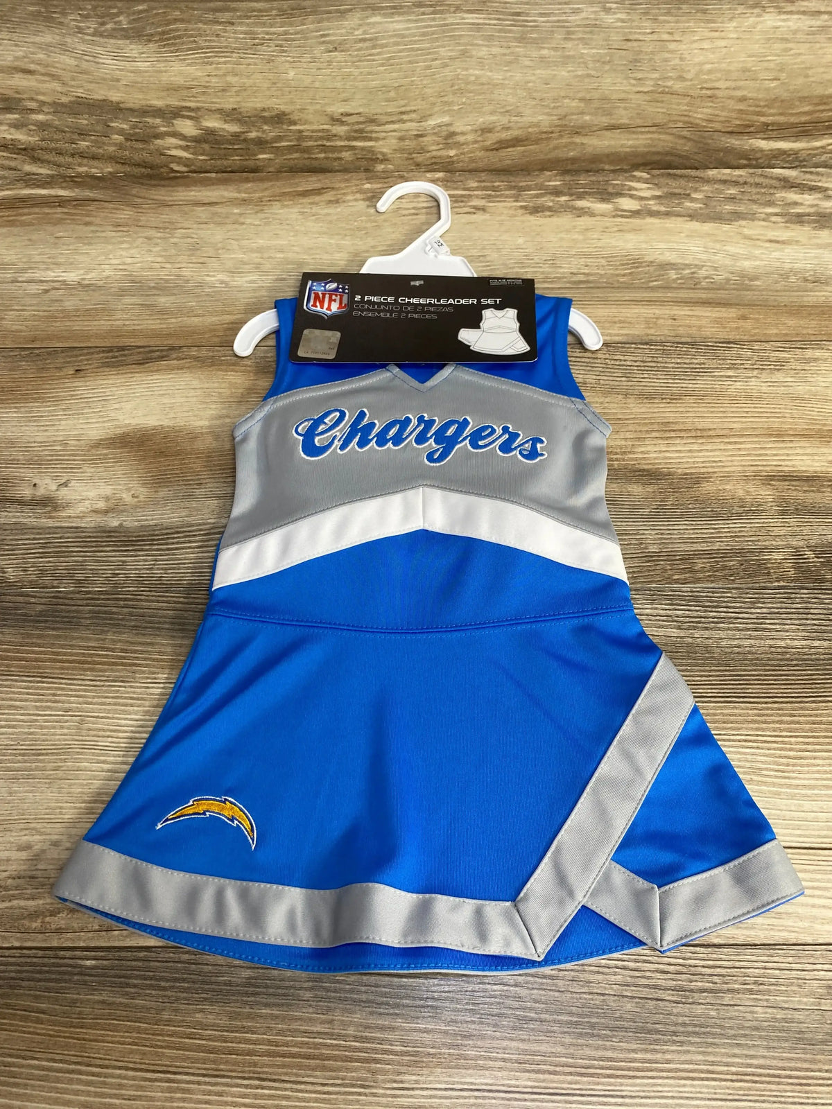 Flat lay of blue Chargers cheerleader dress with script on chest, silver chevron trim and lightning bolt patch on wood
