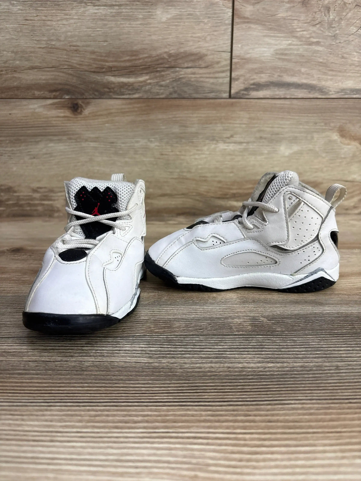 Pair of white and black toddler Jordan sneakers on wooden surface, kids resale shoes