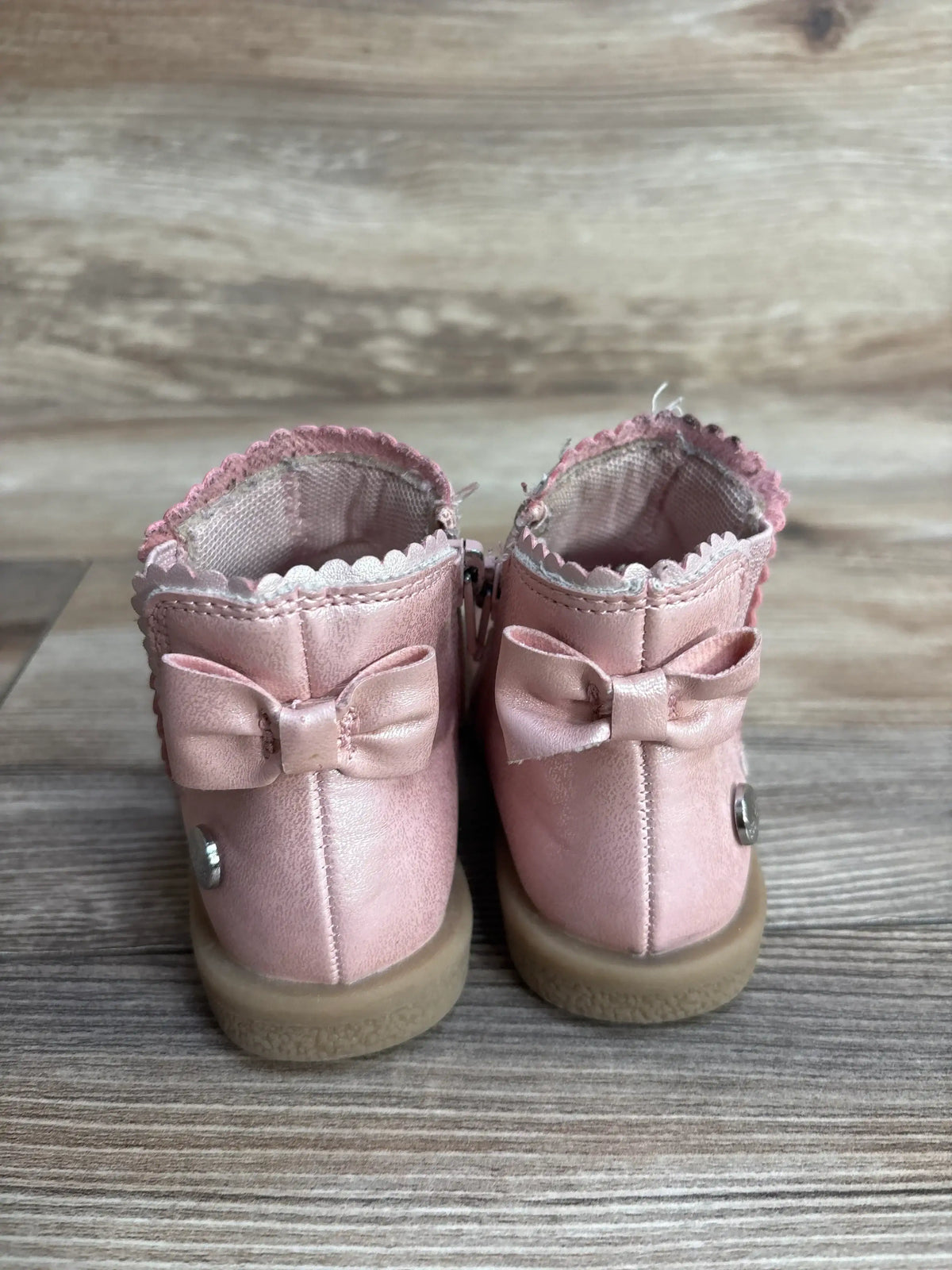 Rear view of Nicole Miller pink toddler ankle boots, size 6C, showing back bows, scalloped trim, and tan soles on a wooden floor