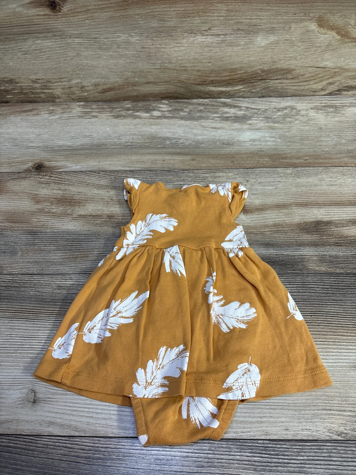 Yellow Carter's baby bodysuit dress with white leaf prints on a wooden background