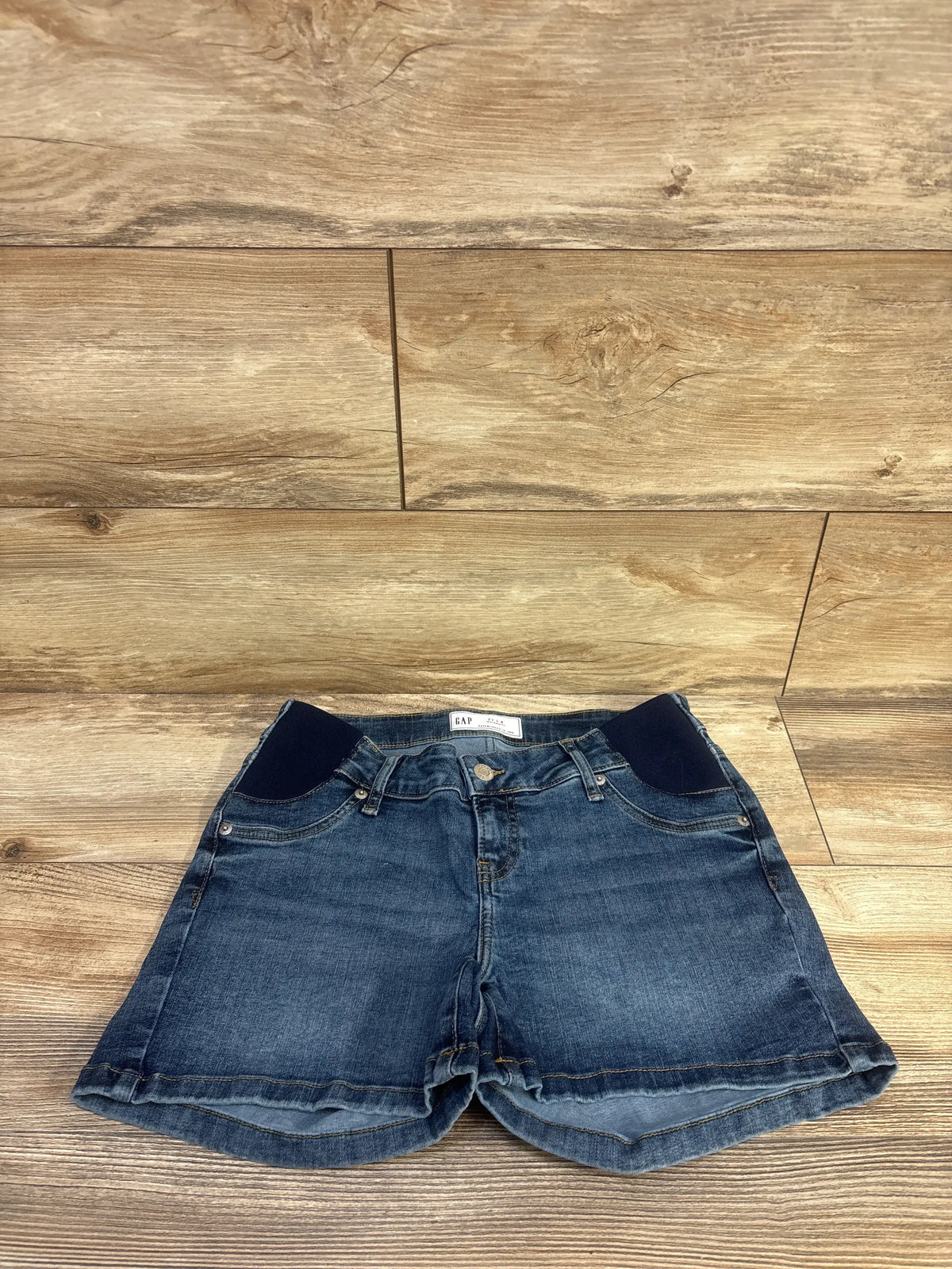 Front view of Gap maternity denim shorts showcasing dark wash stretch denim and four inch inset panel on a wood floor