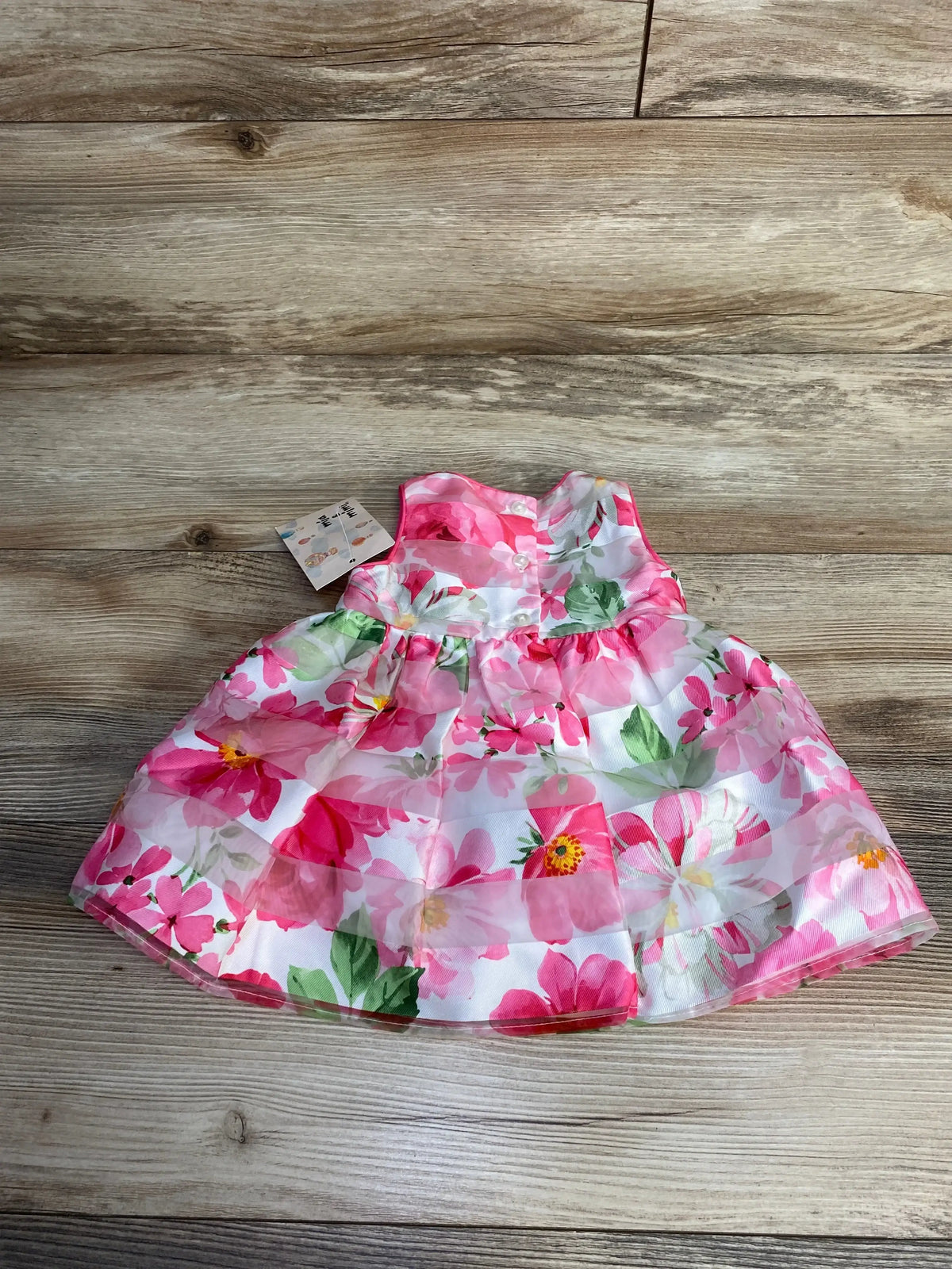 Top-down view of Mia & Mimi 2-piece baby dress and bloomers showcasing pink floral print and gathered full skirt on wood background
