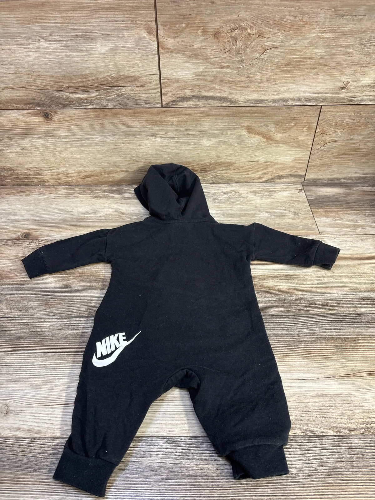 Front view of Nike black hooded coverall showcasing long sleeves, hood, and white logo on a wood floor