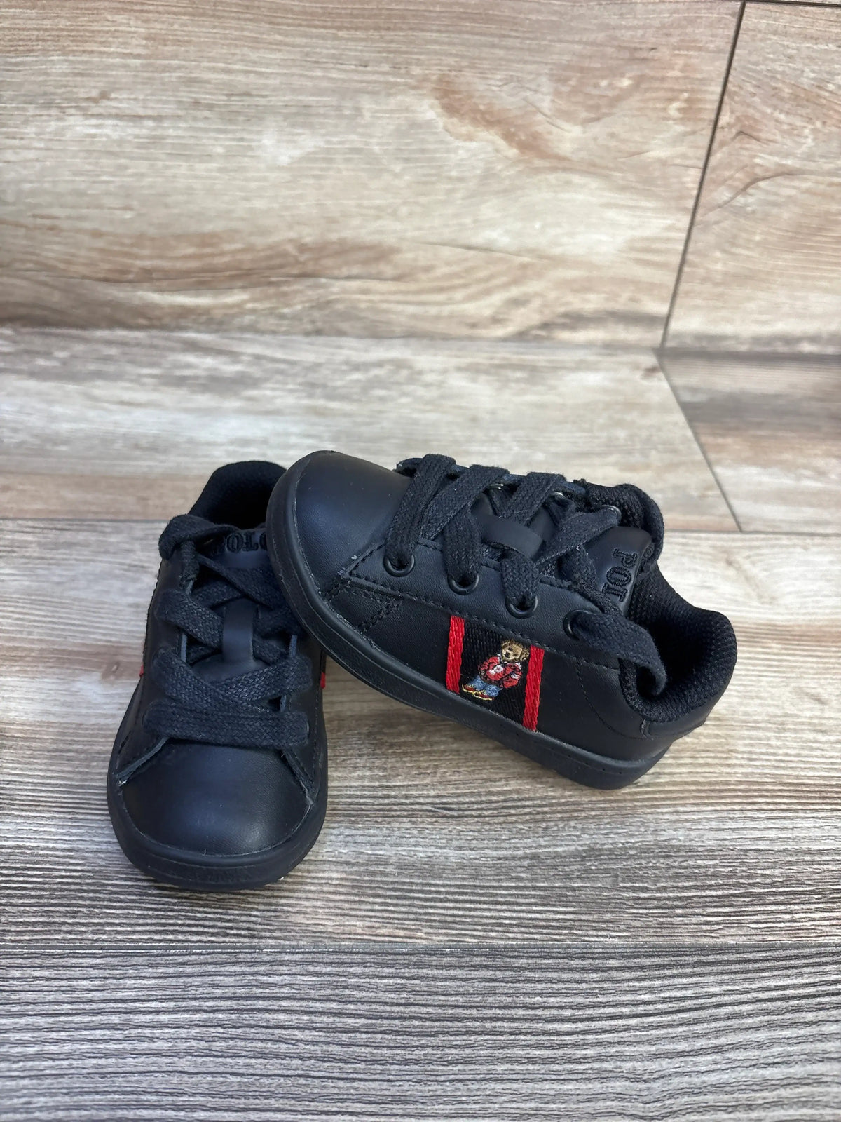 Angled view of black Polo Ralph Lauren Quilton Bear sneakers showcasing embroidered Polo Bear and lace-up styling on wood-look flooring