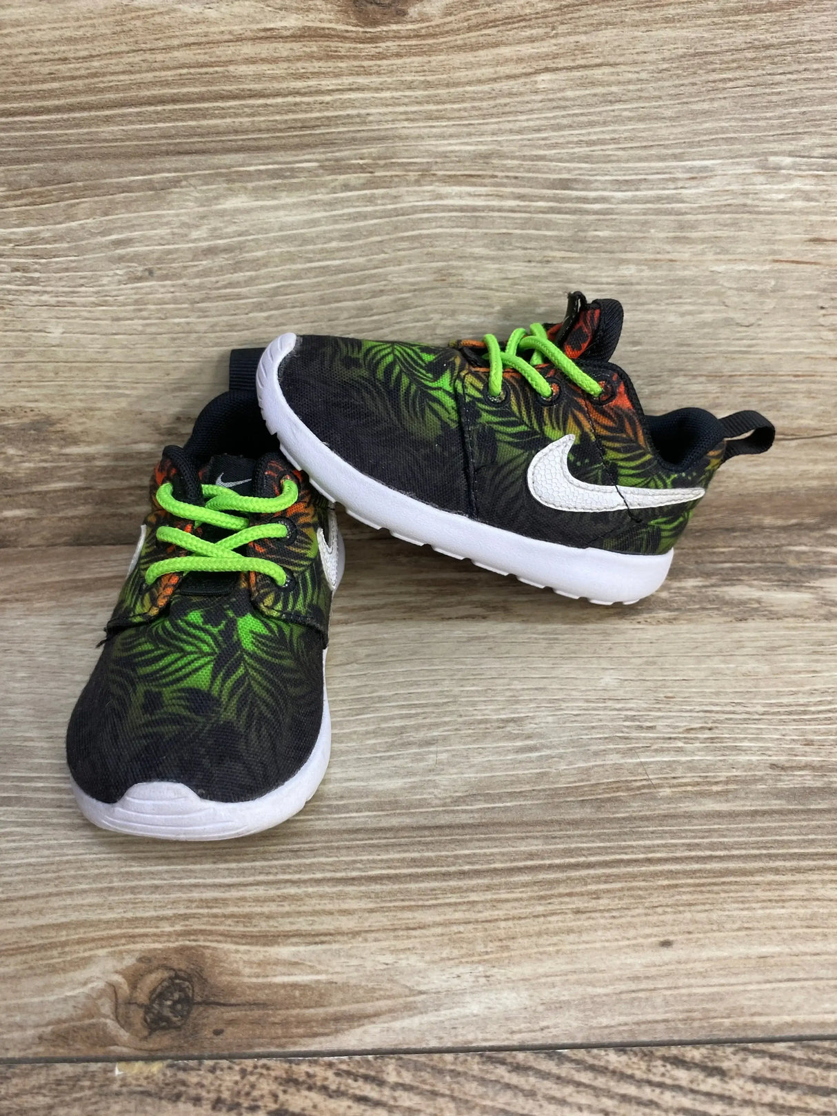 Side and front view of Nike Roshe Run sneakers with green tropical print, neon green laces, white swoosh on wood background