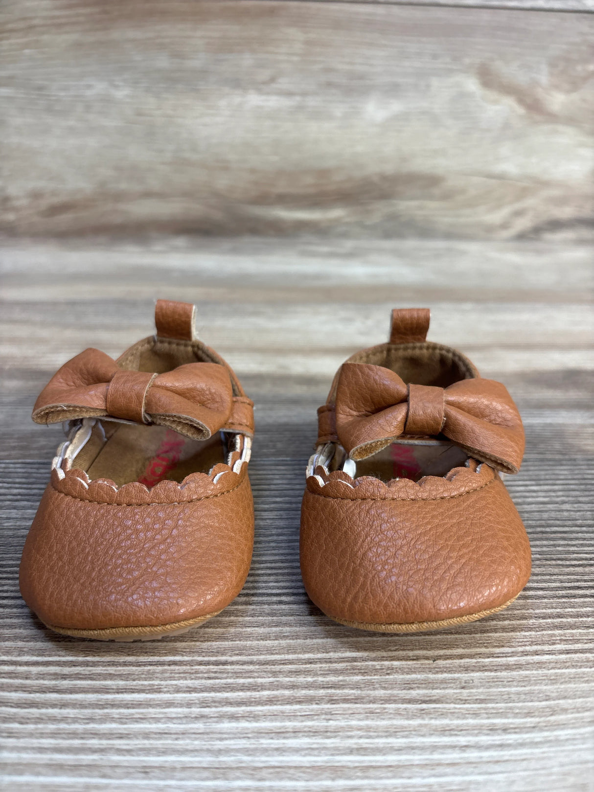 Brown baby moccasins with bows, textured leather, on wood background, kids footwear resale