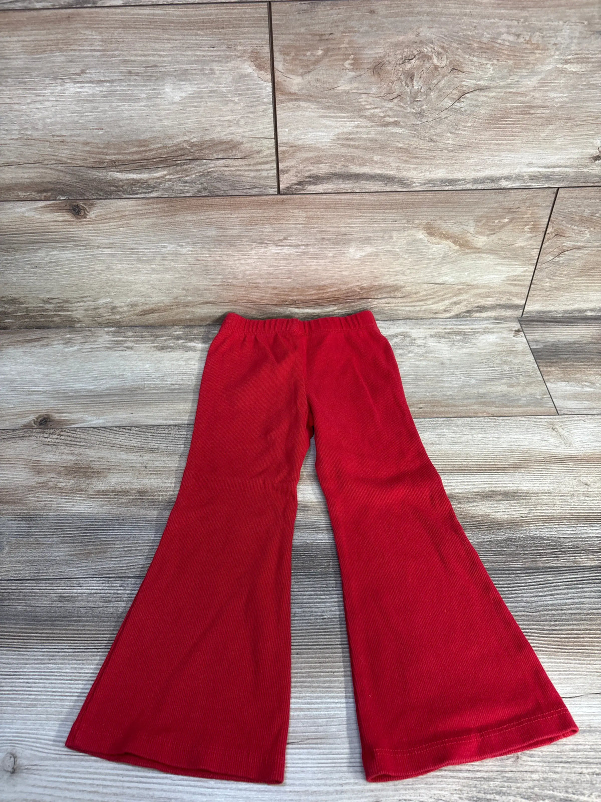 Front view of Baby Gap ribbed flare leggings in red, showcasing flared legs and ribbed fabric on a wood-look background