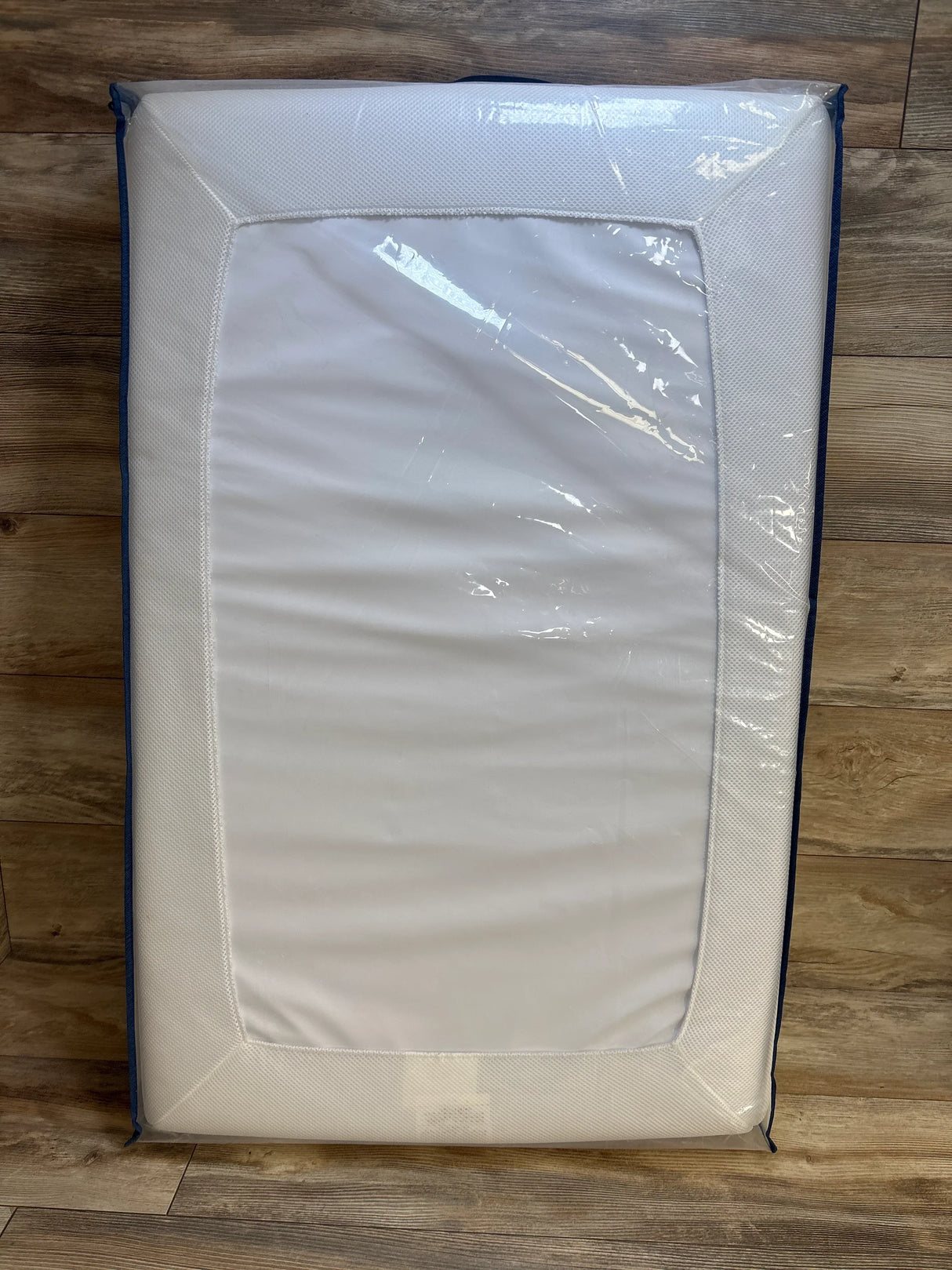 Top view of Moonlight Slumber mini crib mattress, white surface with mesh sides and blue trim, wrapped in clear plastic