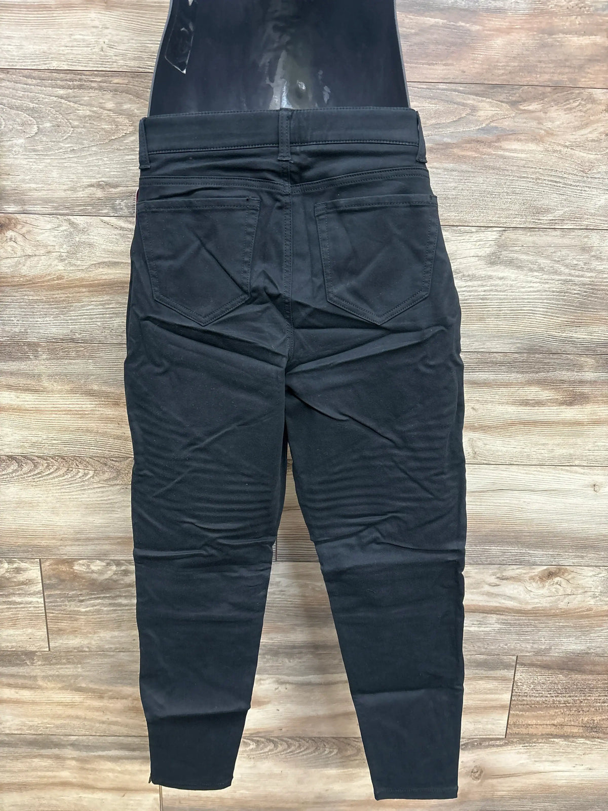 Rear view of black maternity jeggings showing back pockets, tapered legs and elastic belly panel on wood floor